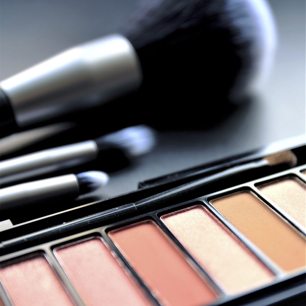 Lidschattenpalette in warmen Farben mit Make-up-Pinseln auf dunkler Oberfläche.