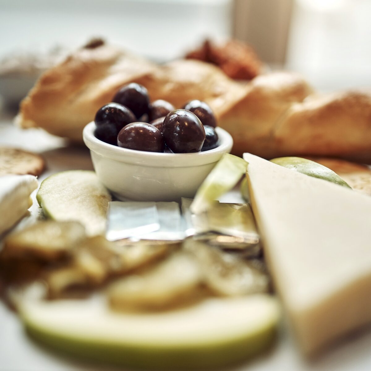 Teller mit Käse, Oliven, Brot und Obstscheiben, arrangiert für ein stilvolles Frühstück.