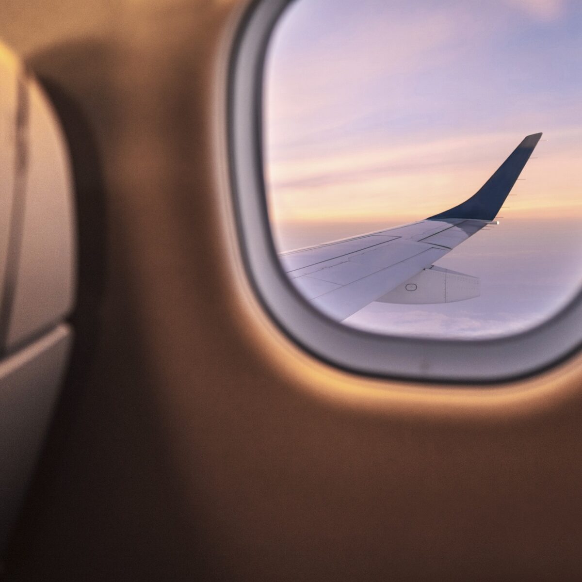 Blick aus Flugzeugfenster bei Sonnenuntergang, Flügel und Himmel im Hintergrund sichtbar.