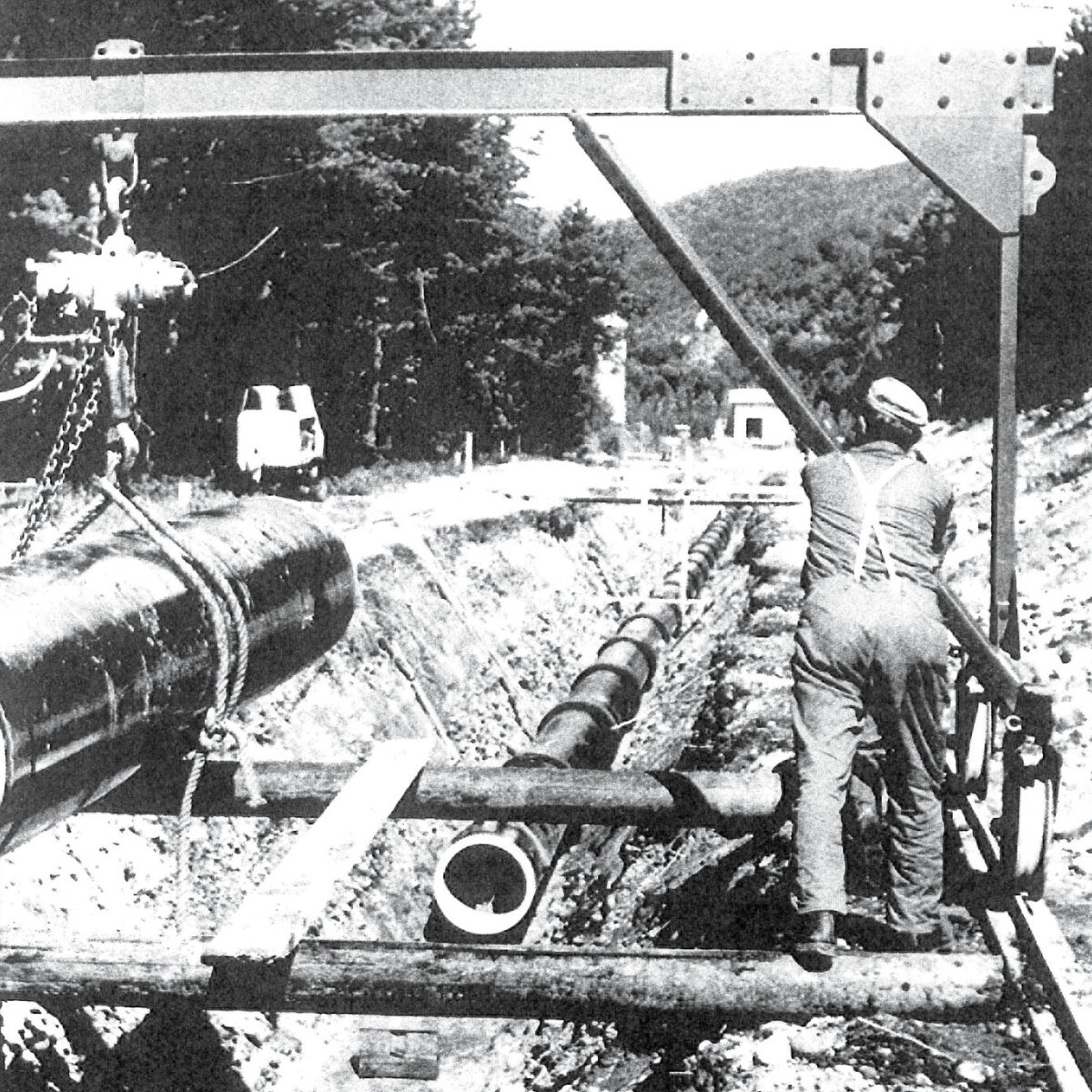 Schwarz-weiß-Aufnahme eines Arbeiters, der Wasserleitungsrohre verlegt