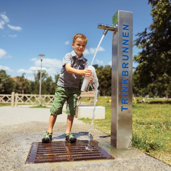 Buf füllt eine Flasche an einem Trinkbrunnen in einem Park bei sonnigem Wetter.