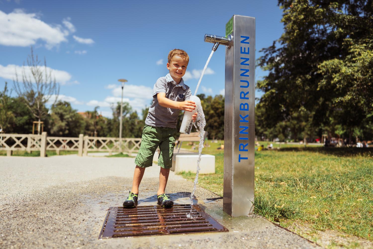 Buf füllt eine Flasche an einem Trinkbrunnen in einem Park bei sonnigem Wetter.