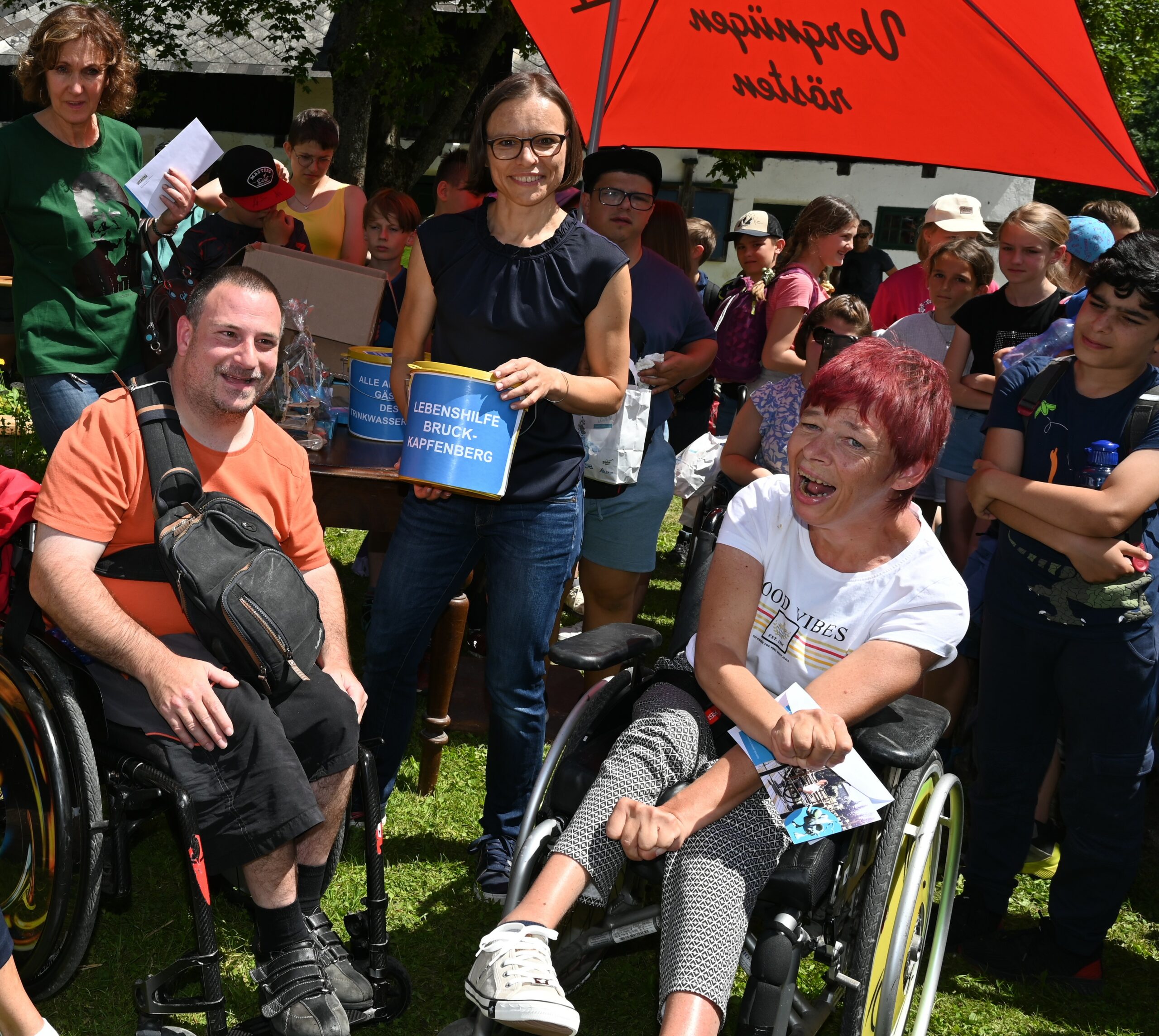 Menschen bei Preisverleihung im Freien, zwei Personen im Rollstuhl, lachend und fröhlich.