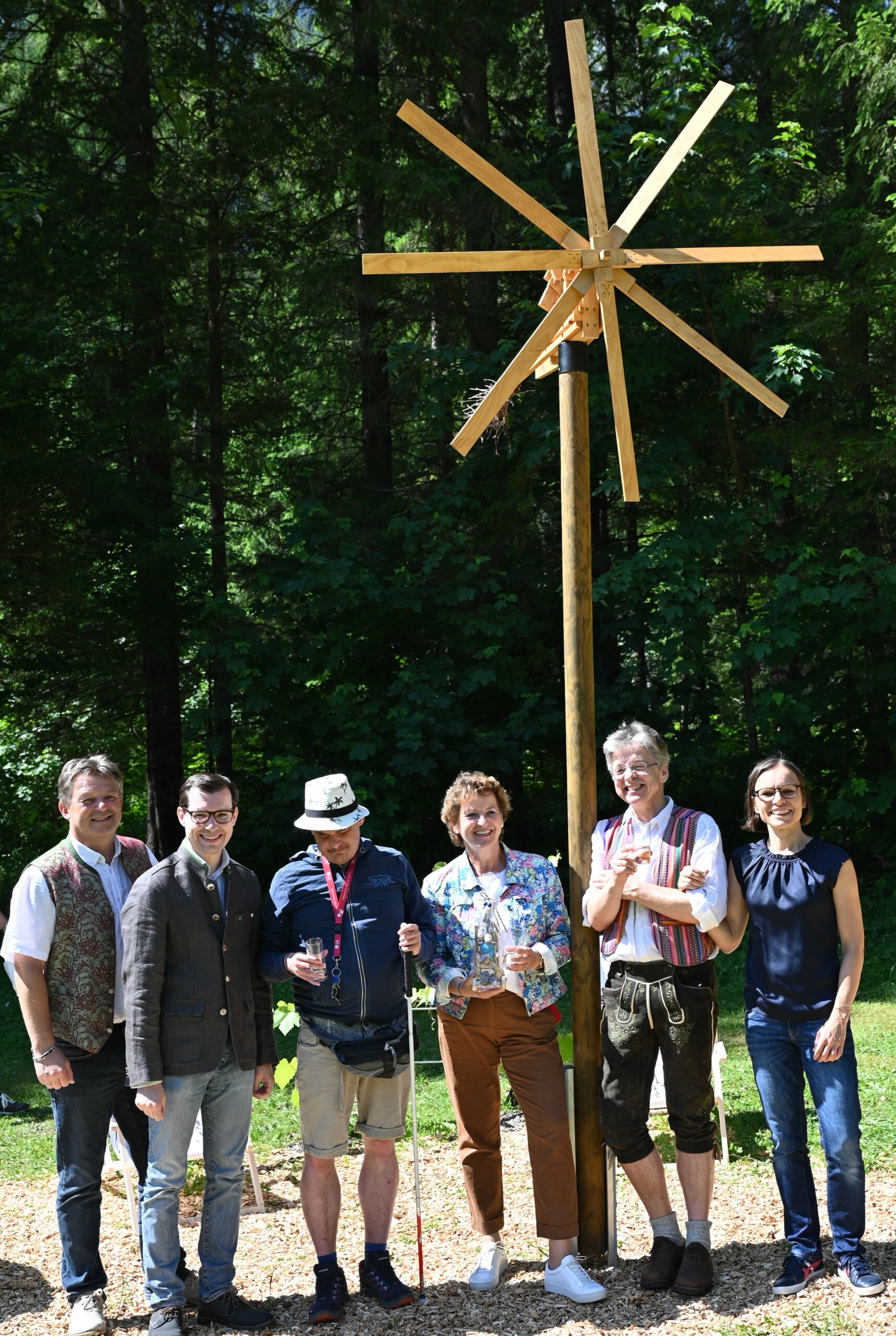Gruppe vor einem hölzernen Stern, umgeben von Wald, bei einer Veranstaltung im Freien.