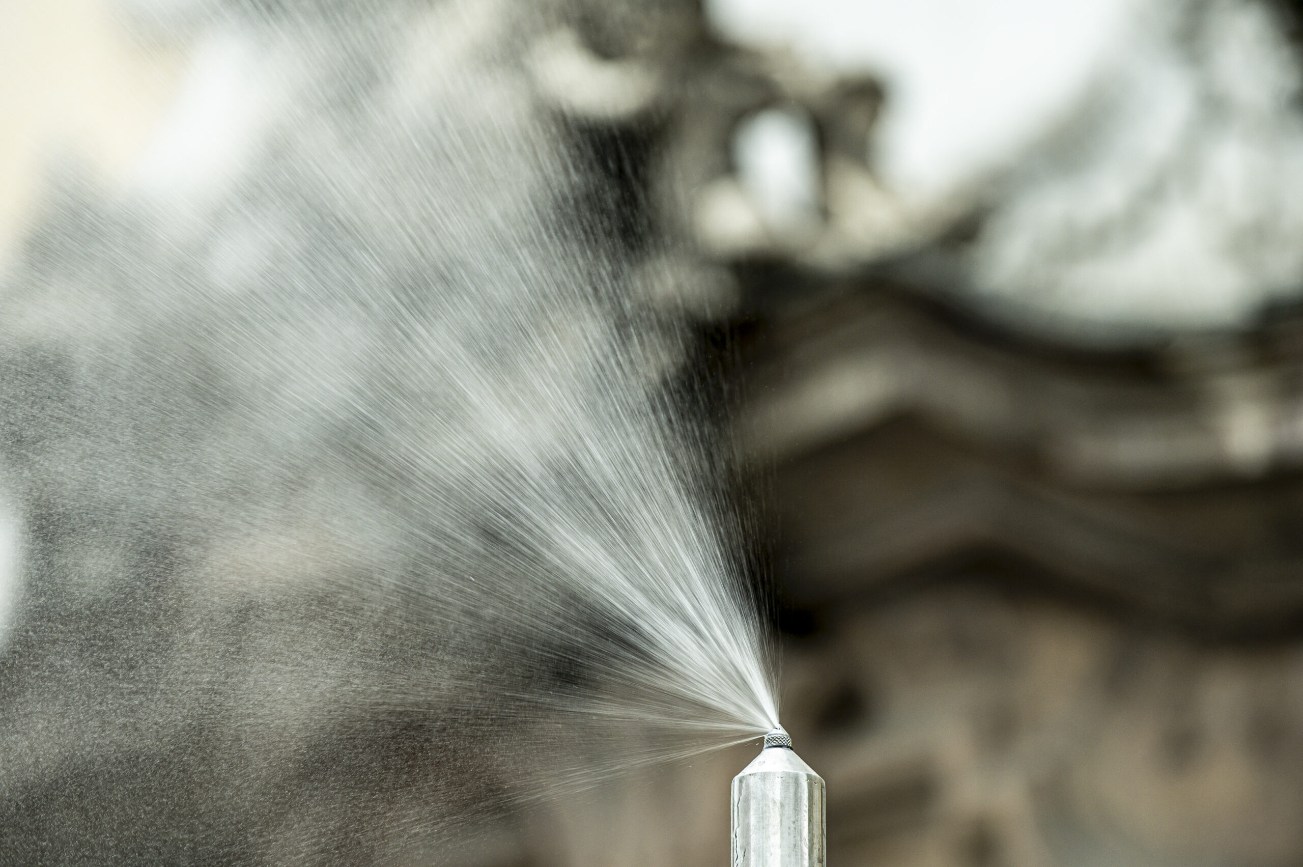 Detailaufnahme einer Düse, die feinen Wassernebel versprüht, unscharfer Hintergrund.