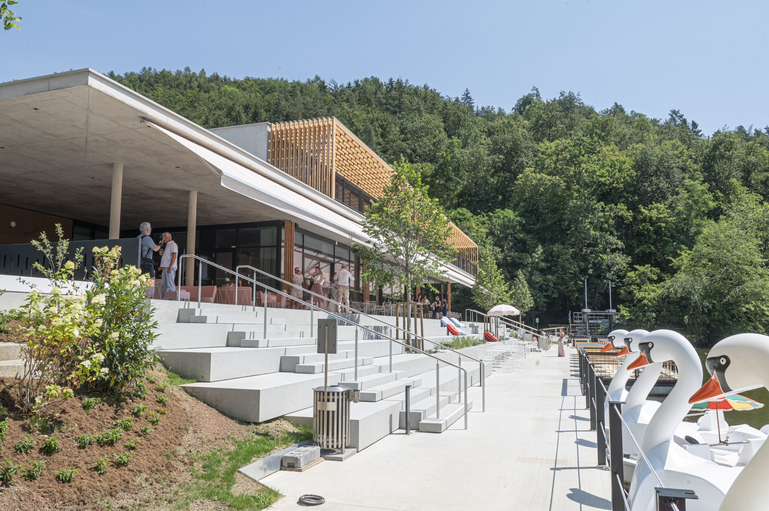 Neues Waldcafé Thalersee mit moderner Terrasse, Stufen und Tretbooten vor grüner Waldkulisse.