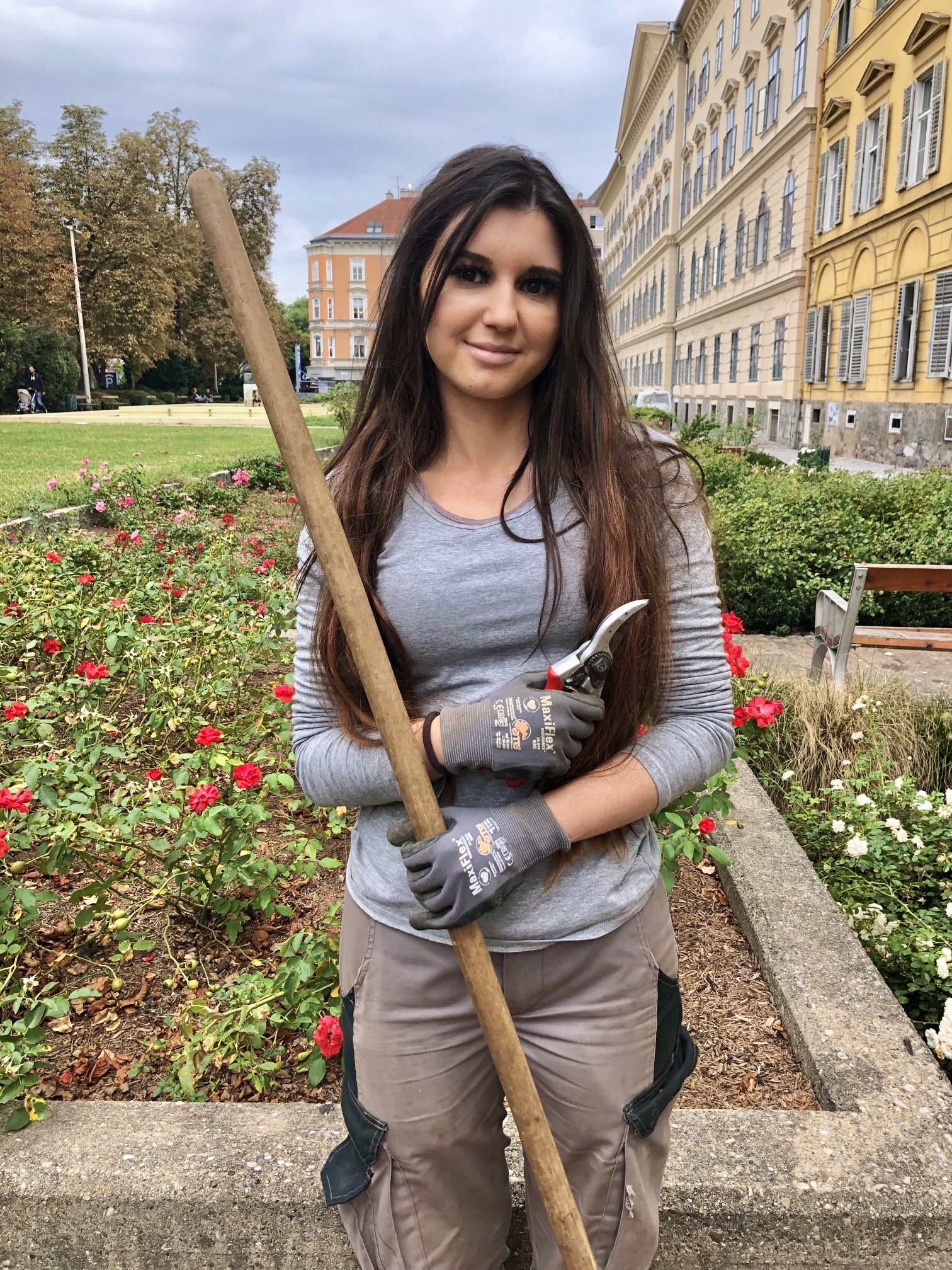 Lehrling Elena Gunzer mit Arbeitsgeräten im Rosengarten, umgeben von gepflegten Grünflächen.