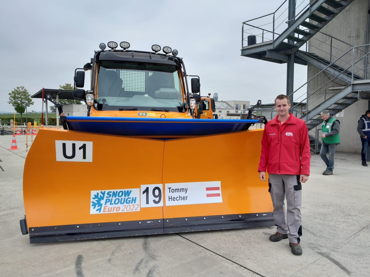 Tommy Hecher steht vor Schneepflug mit Aufschrift 'Snow Plough Euro 2022' und Österreich-Flagge.