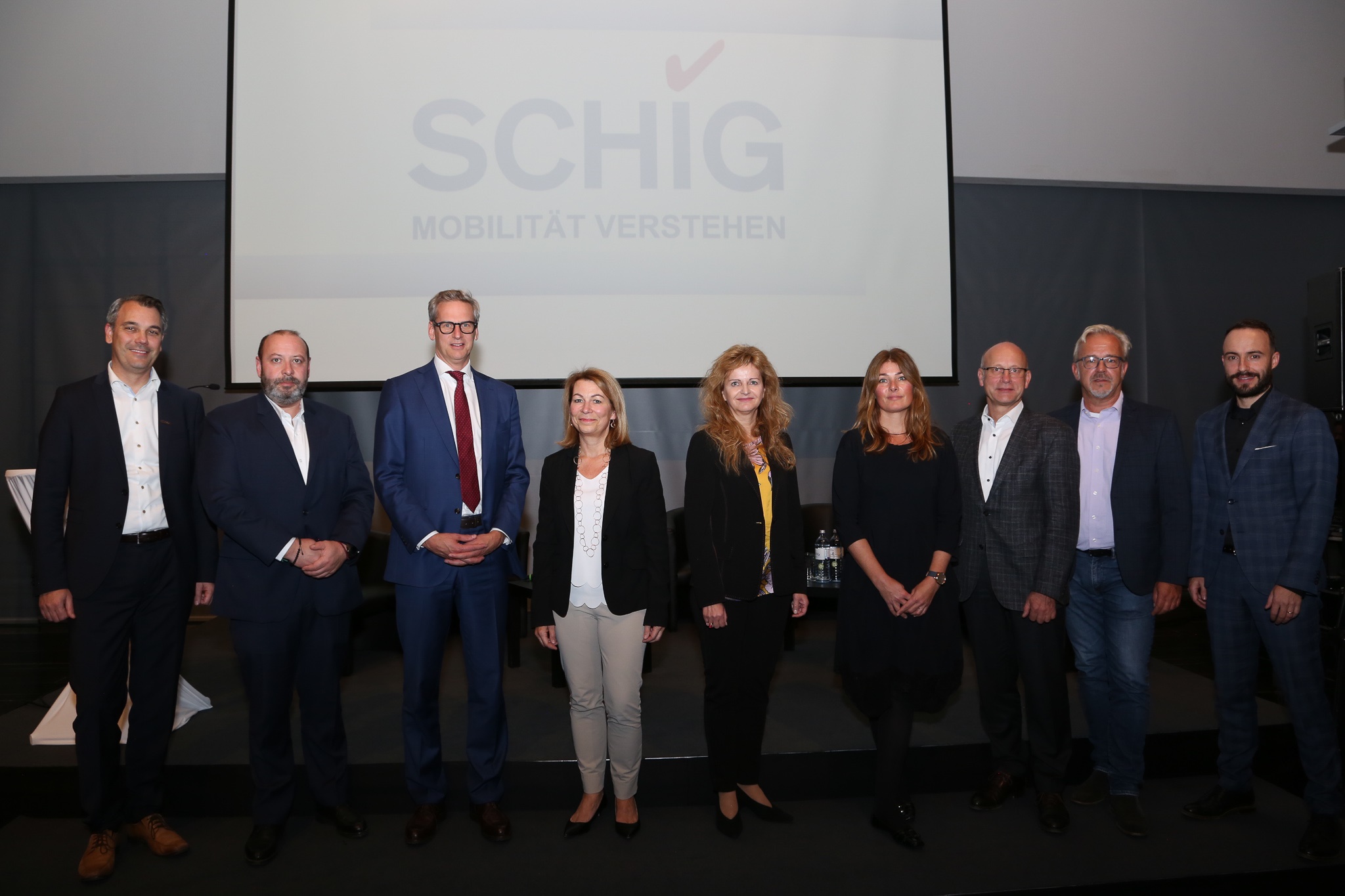 Gruppe vor SCHIG-Logo, Experten diskutieren innovative Lösungen für moderne Mobilität.