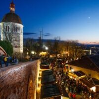 Weihnachtsmarkt am Schloßberg mit Blick auf Graz bei Sonnenuntergang und festlicher Beleuchtung.