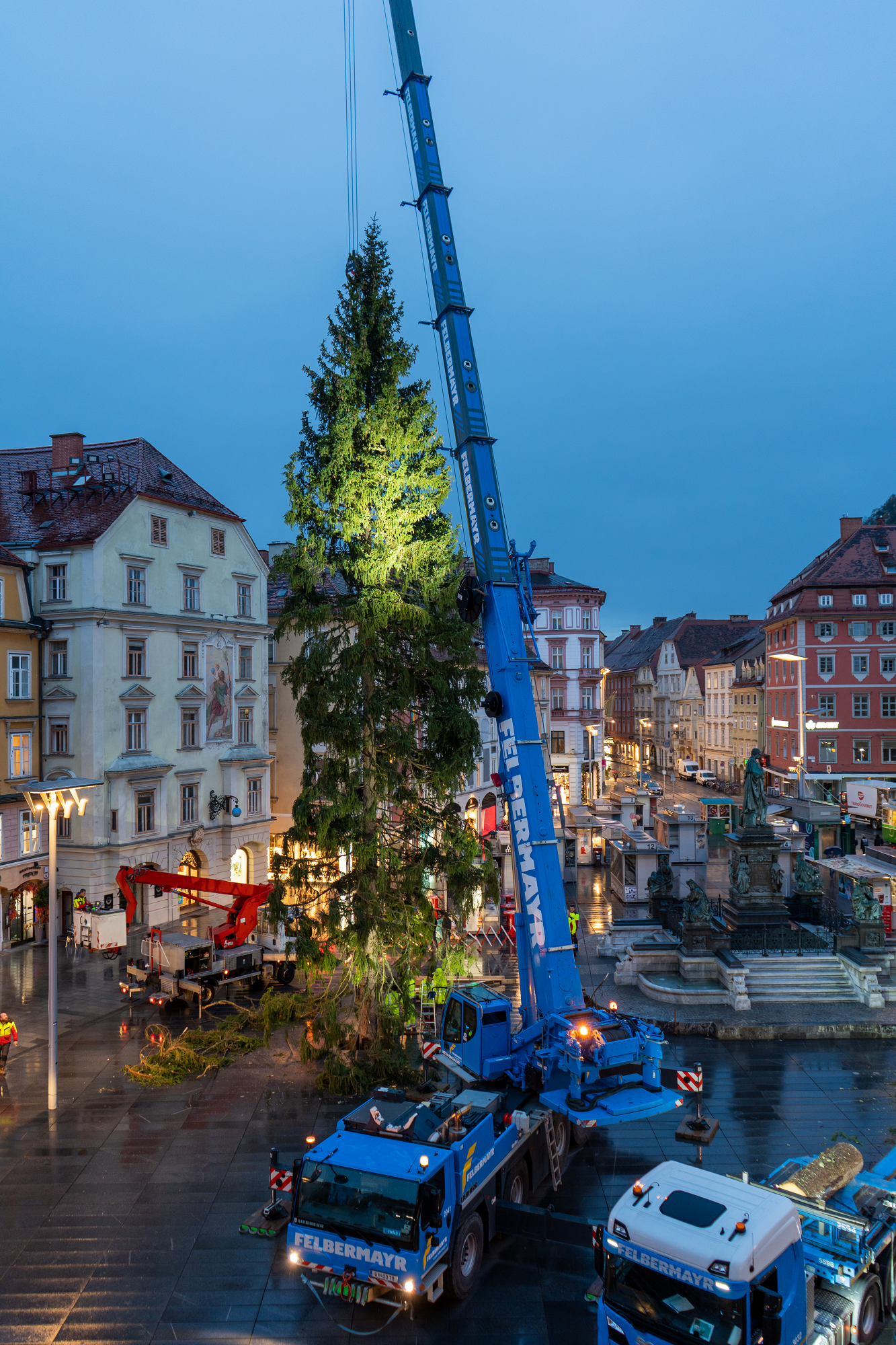 A crane lifts a Christmas tree into place in Graz's main square. The crane is labeled "Felbermayr".