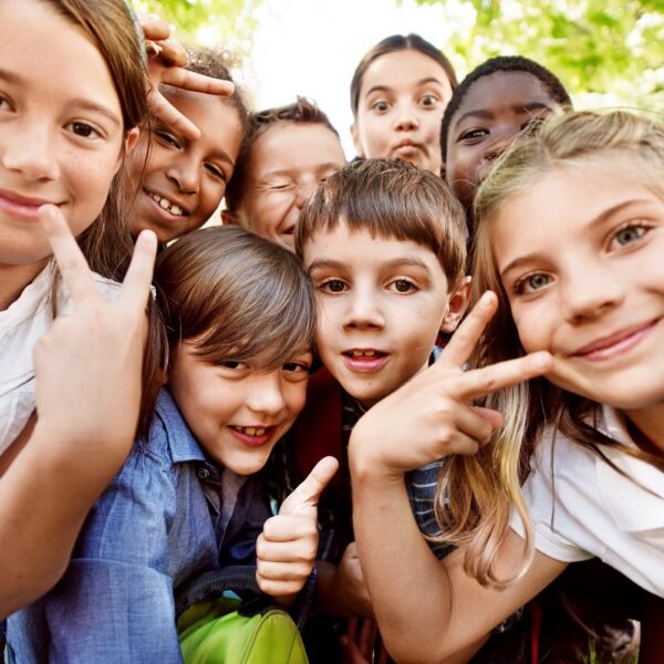 Gruppe lachender Kinder macht ein Selfie im Freien unter grünen Bäumen an sonnigem Tag