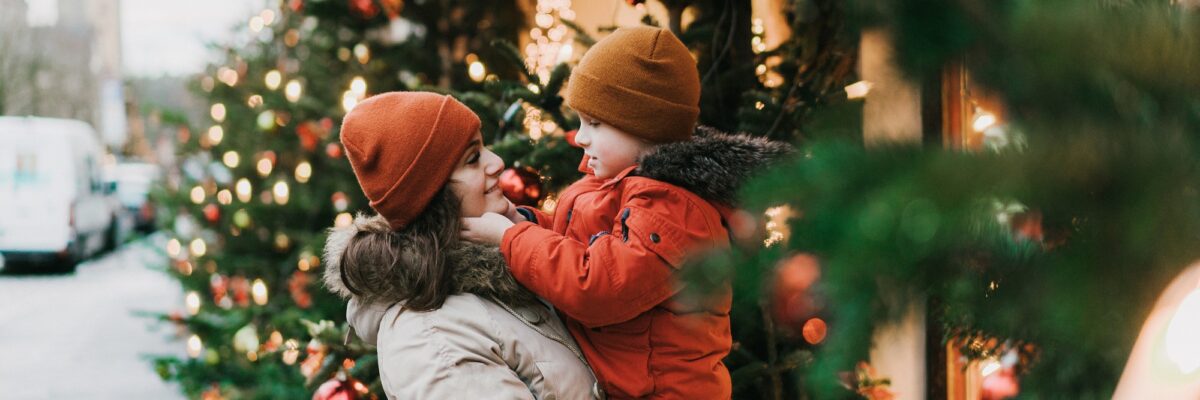 Junge Frau trägt Kind am Arm, im Hintergrund weihnachtlich dekoriertes Geschäft