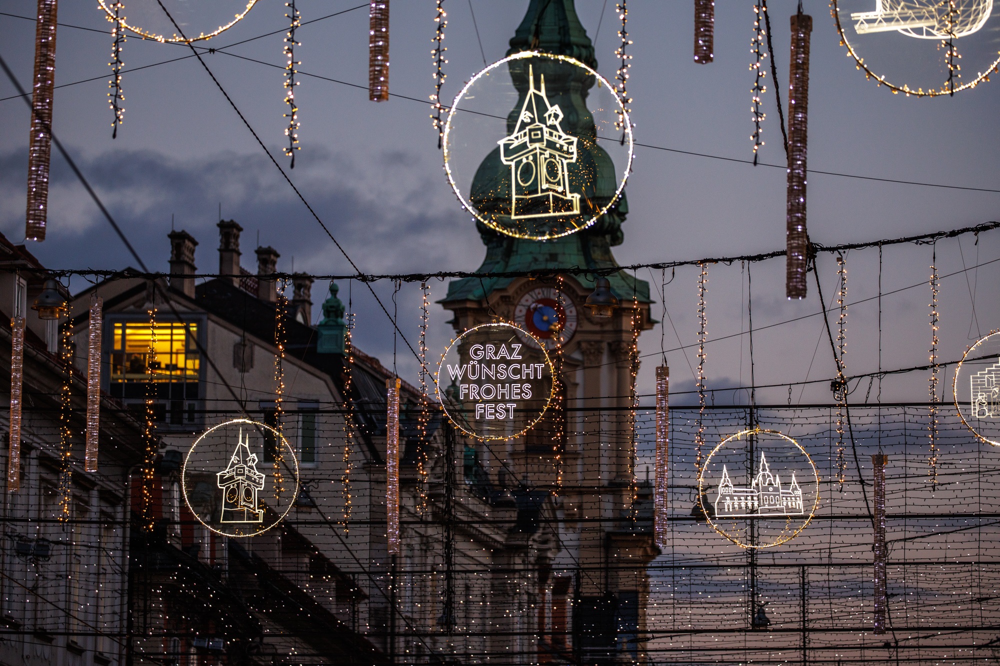 Weihnachtsbeleuchtung in Herrengasse mit hellen Motiven und Schriftzug "Graz wünscht Frohes Fest"