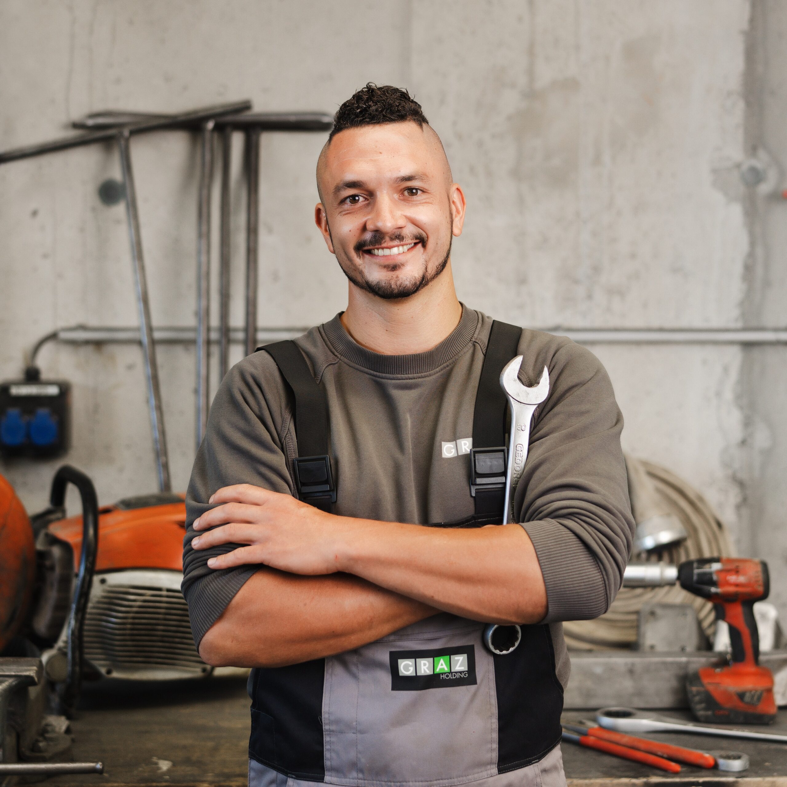Lächelnder Mechaniker der Holding Graz mit Schraubenschlüssel in Hand steht in Werkstatt.