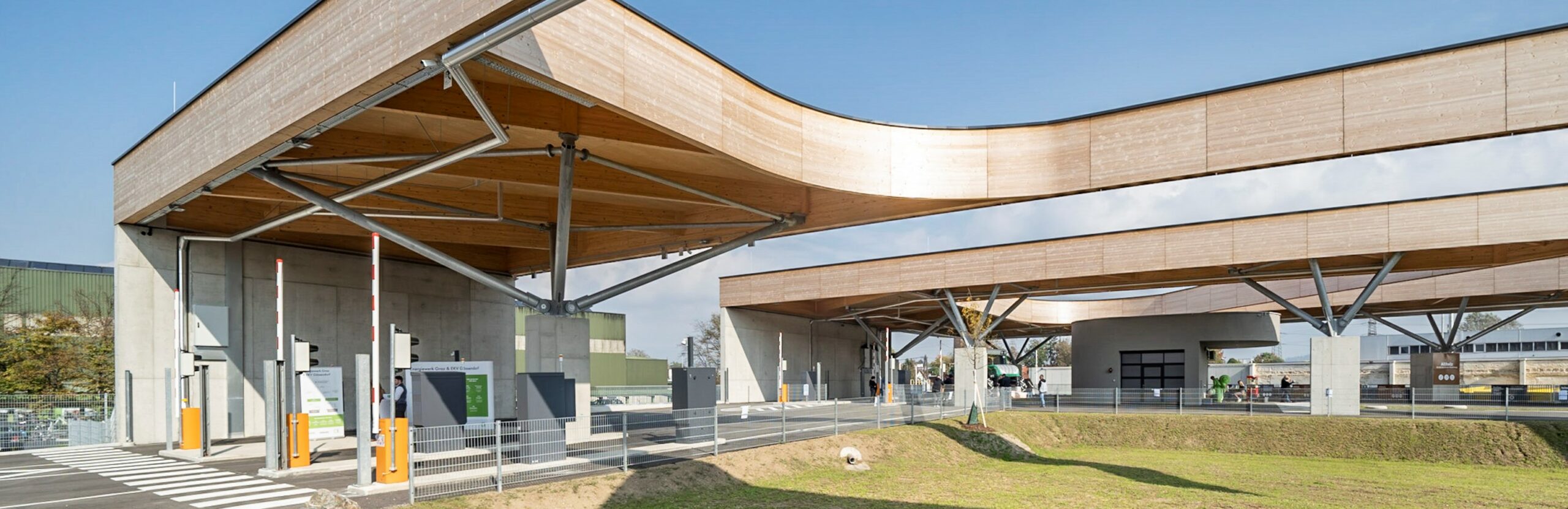 Moderner Ressourcenpark mit geschwungenem Holzdesign und Einfahrt für nachhaltiges Recycling in Graz.