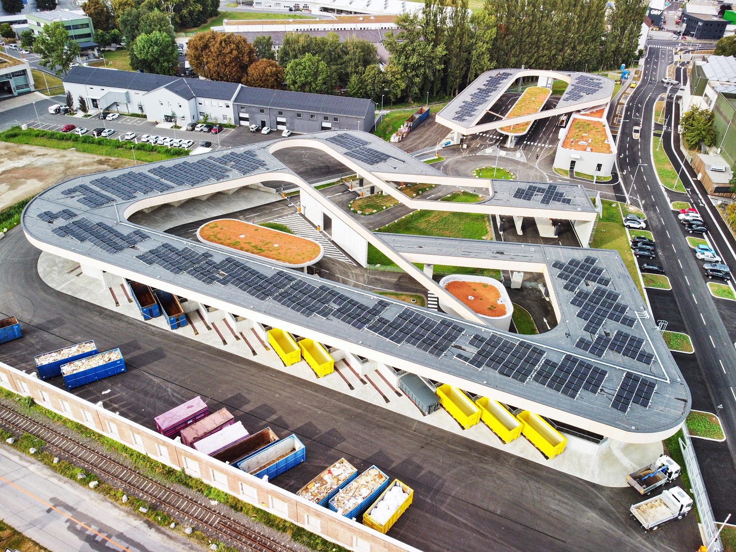 Moderne Recyclinganlage mit Solarpanels auf geschwungenen Dächern und Containern im Freien.