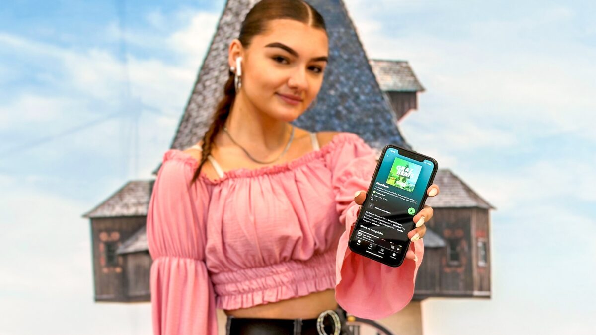 Frau präsentiert Smartphone mit Spotify-App vor Kulisse mit Grazer Uhrturm im Hintergrund.