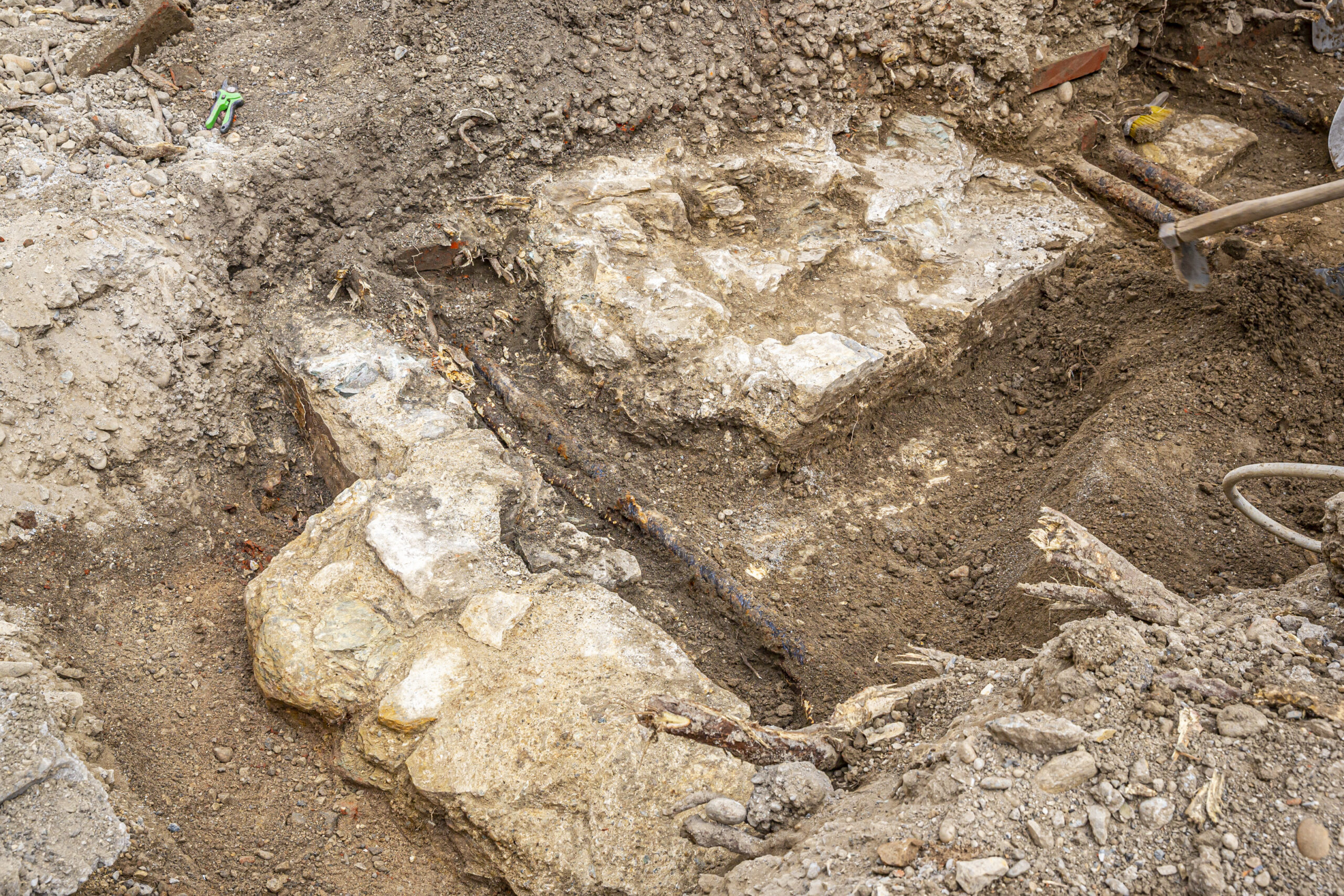 Ausgrabung mit freigelegten Steinen und rostigen Metallrohren in einer Baugrube.