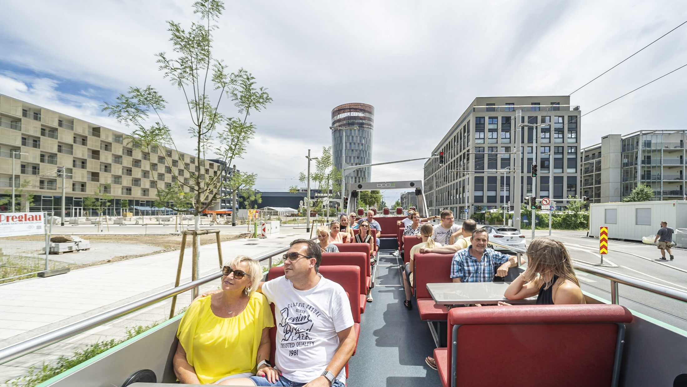 A Graz Linien open-top bus with passengers on a city tour. The bus is driving past modern buildings.