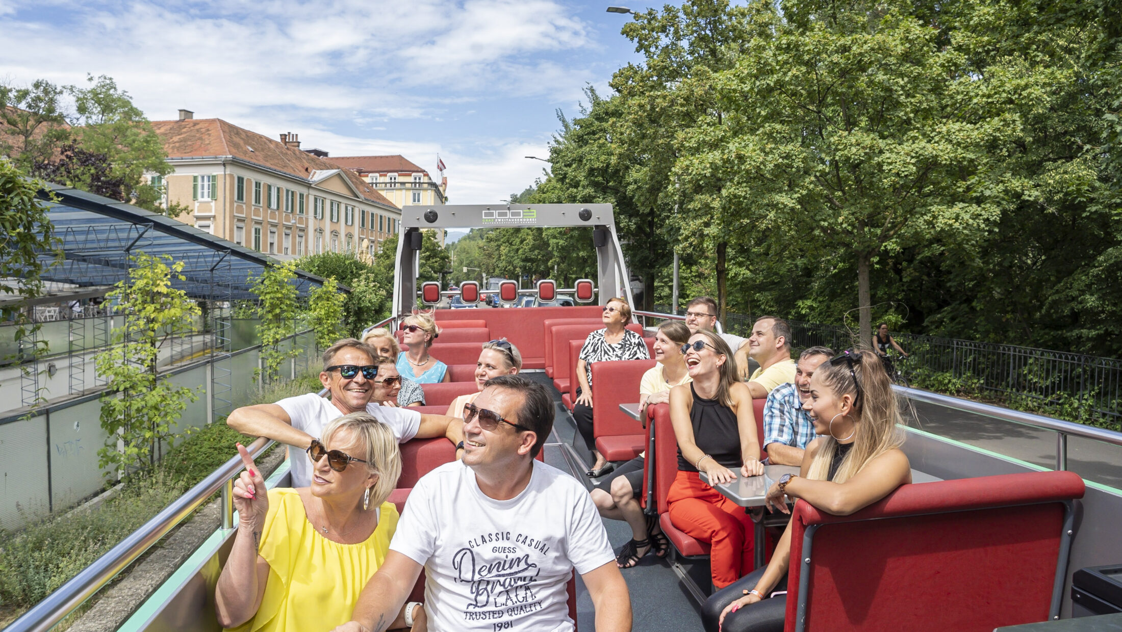 A Graz Linien cabriolet bus with passengers, one wearing a "Classic Casual Denim Brown Black" t-shirt.
