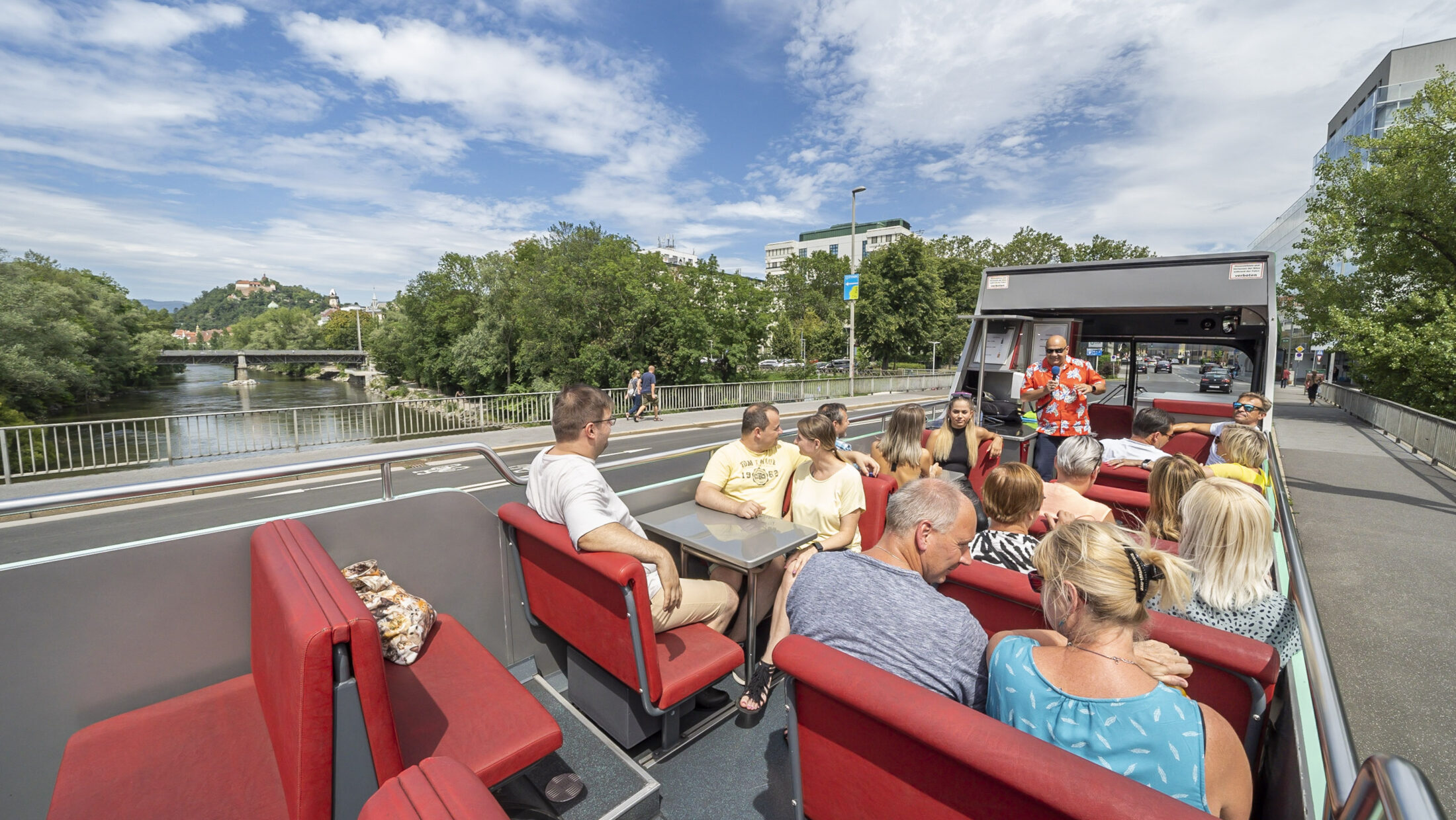 A Graz Linien sightseeing bus with passengers enjoying a tour. A guide stands at the front of the bus.
