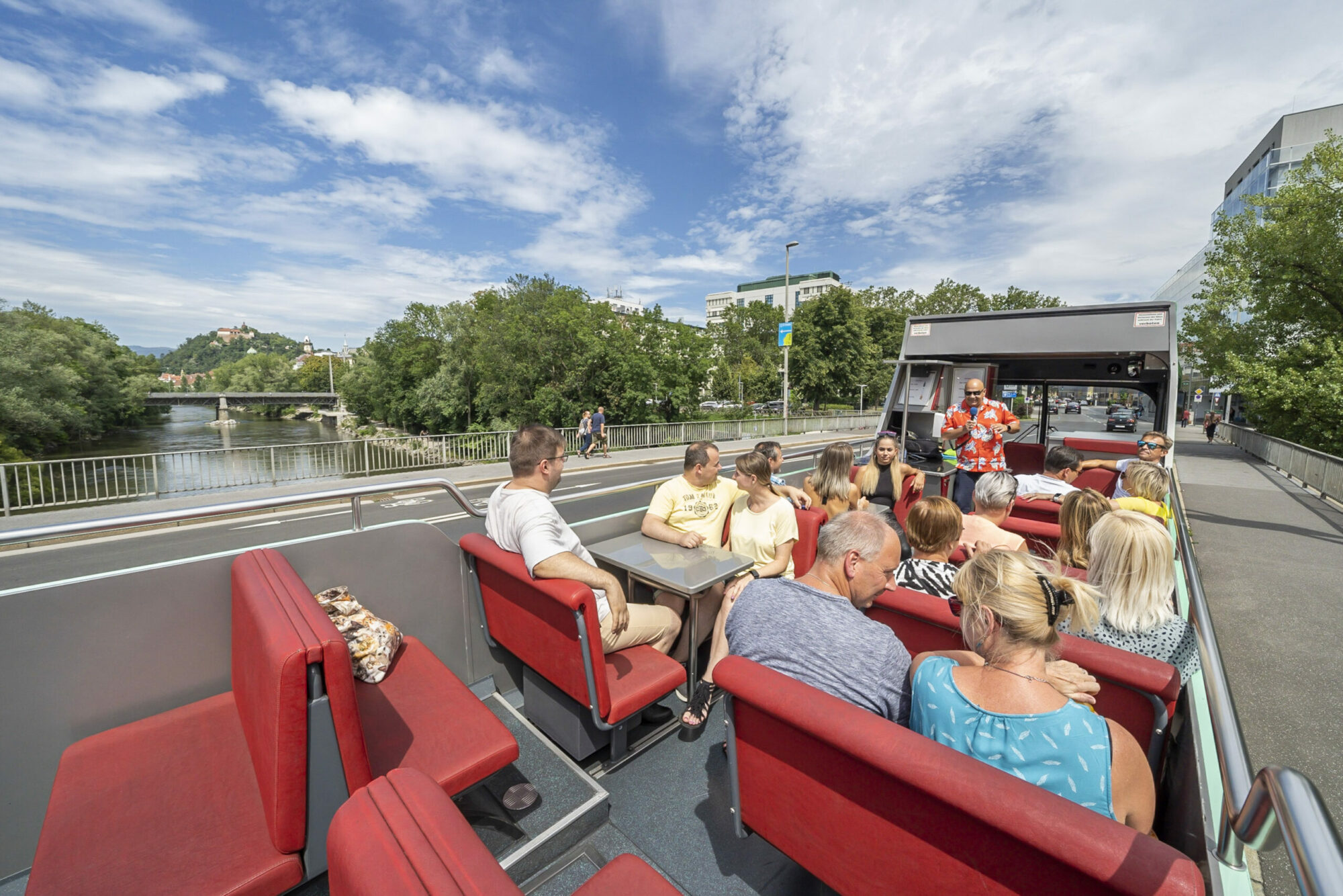 Menschen auf Cabriobus-Tour über Brücke mit Blick auf Fluss und historische Sehenswürdigkeiten.
