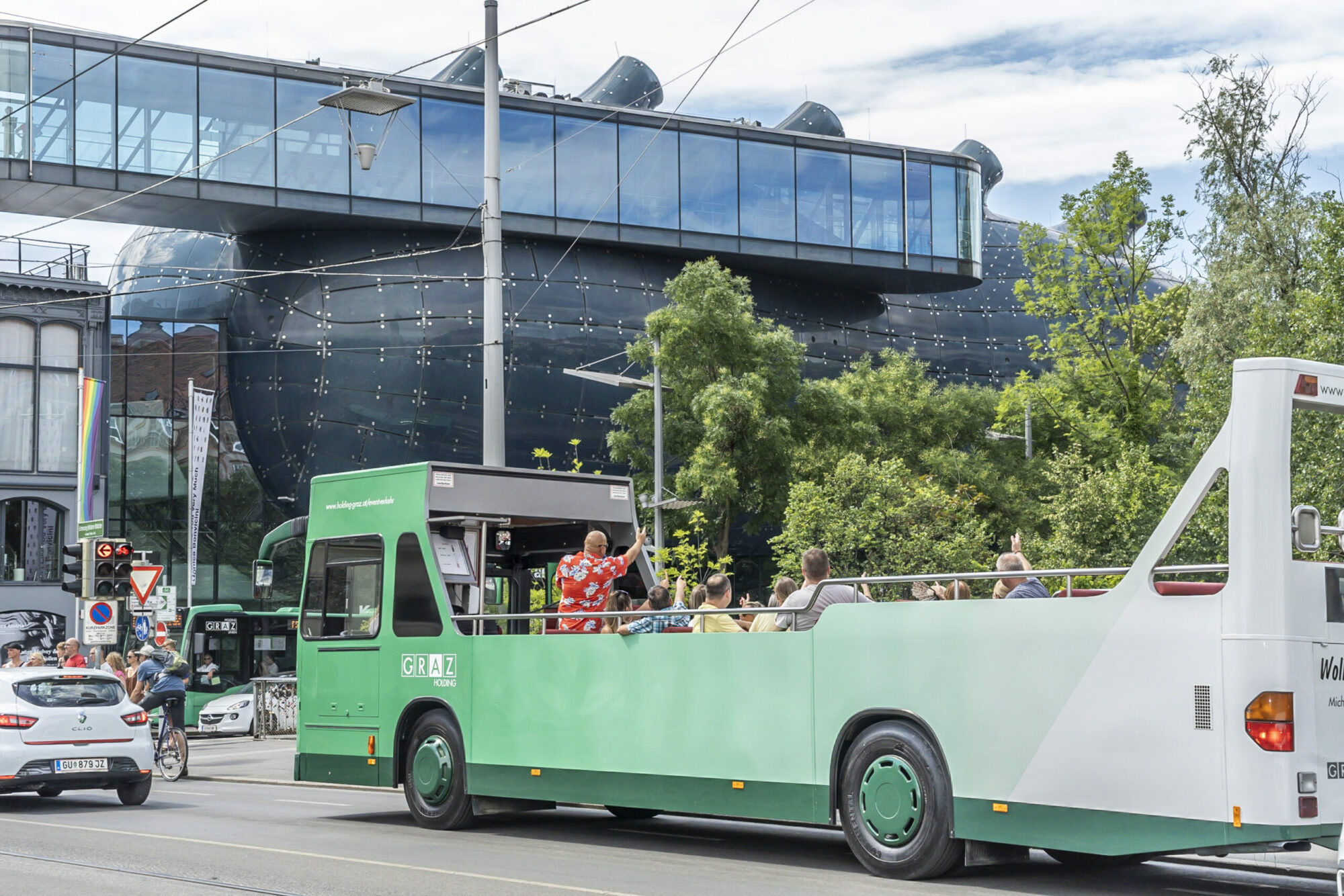 A green and white Graz Linien bus with passengers driving past the Kunsthaus Graz. T