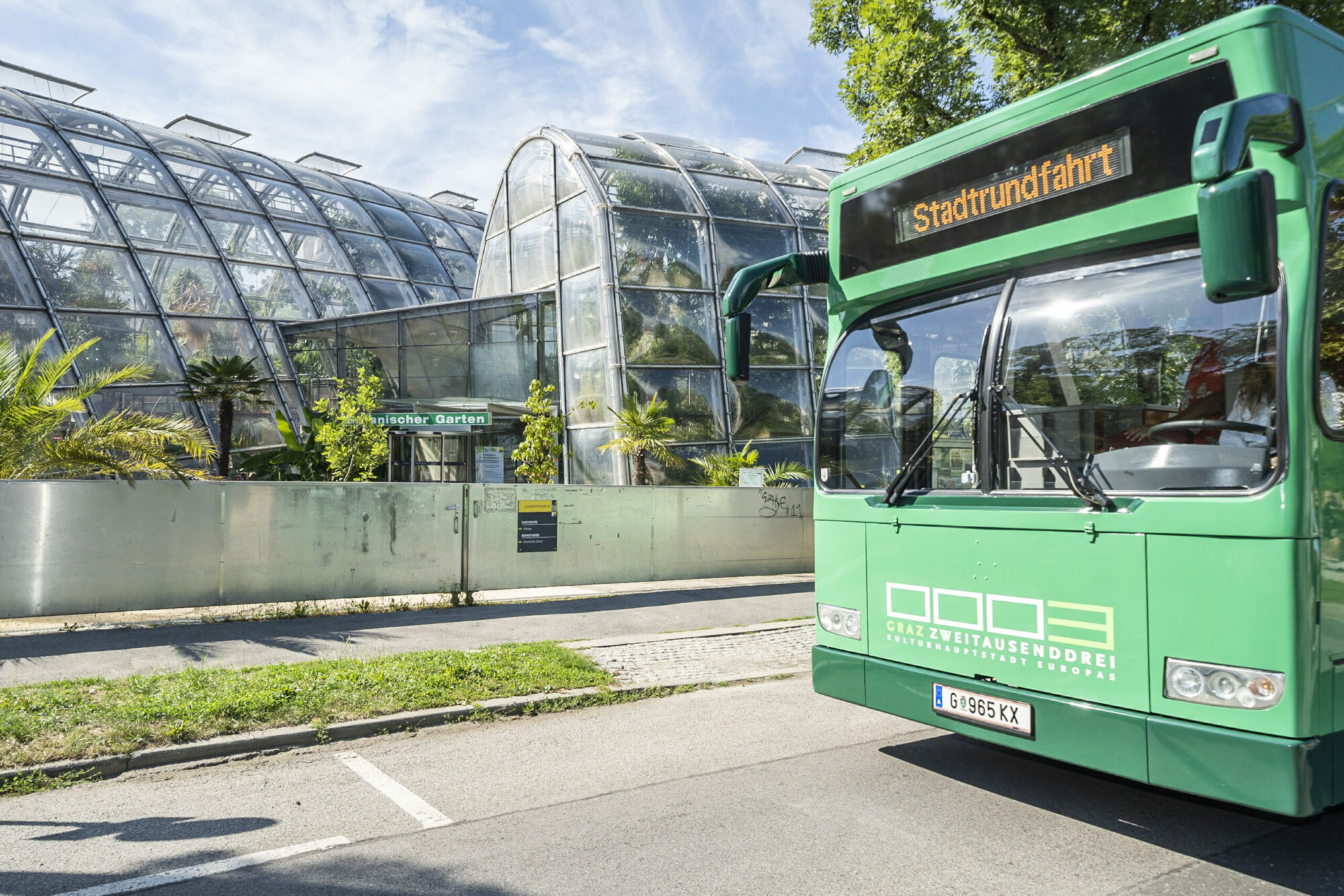 A green Graz Linien bus with "Stadtrundfahrt" on the display, parked in front of a greenhouse