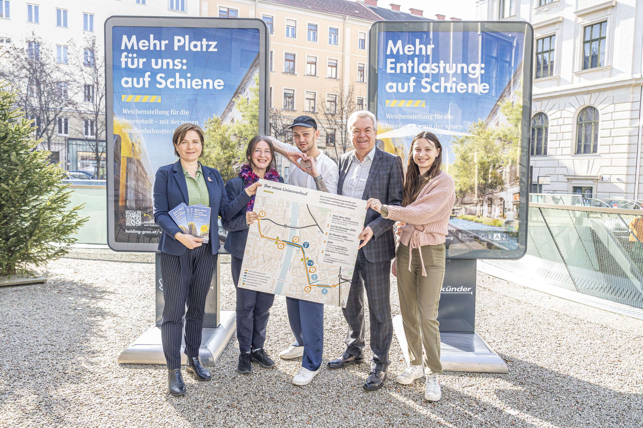 Fünf Personen präsentieren den neuen Linienverlauf der Straßenbahn vor Plakaten in Graz.