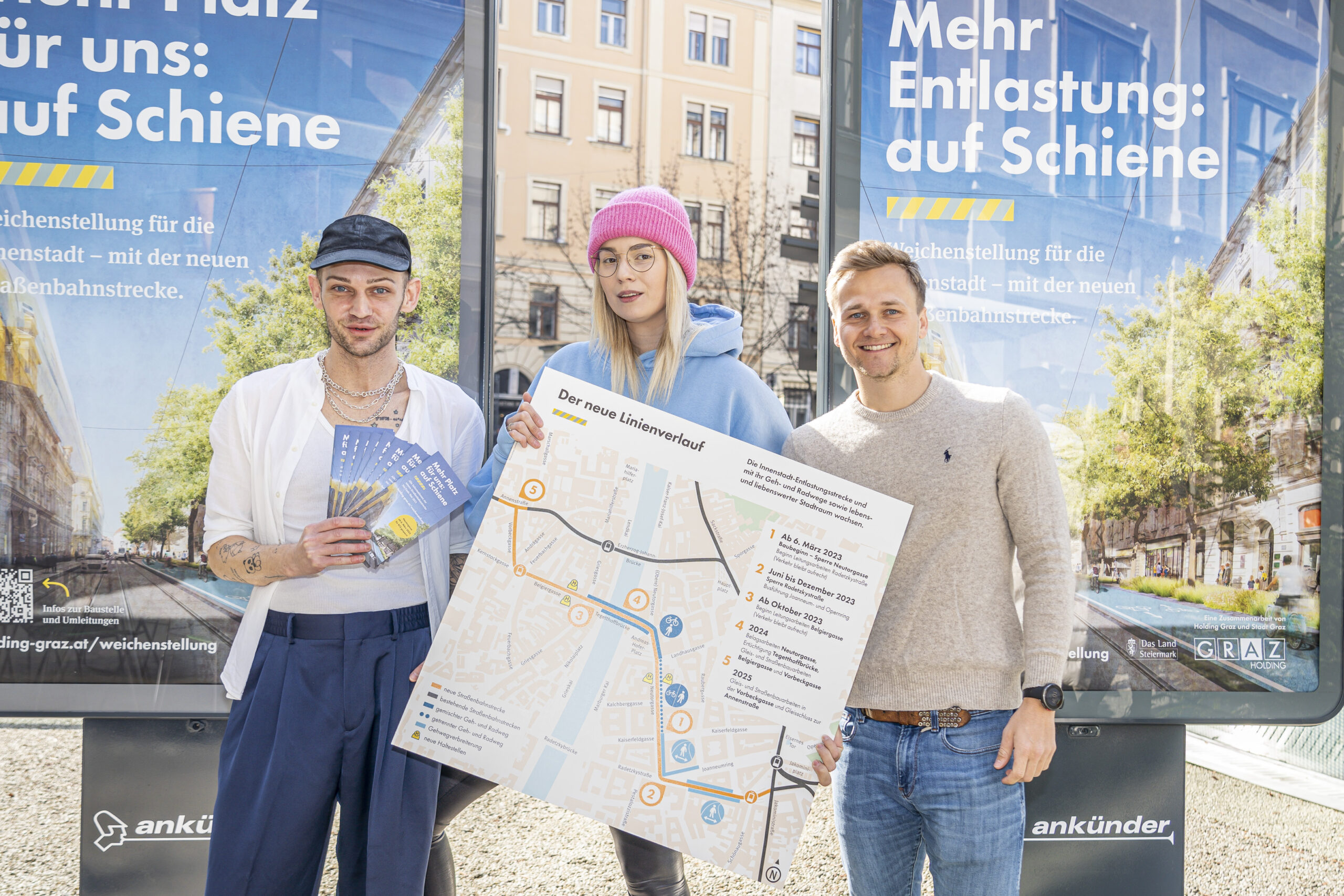 Drei Personen präsentieren den neuen Linienverlauf der Straßenbahn vor Plakaten in Graz.