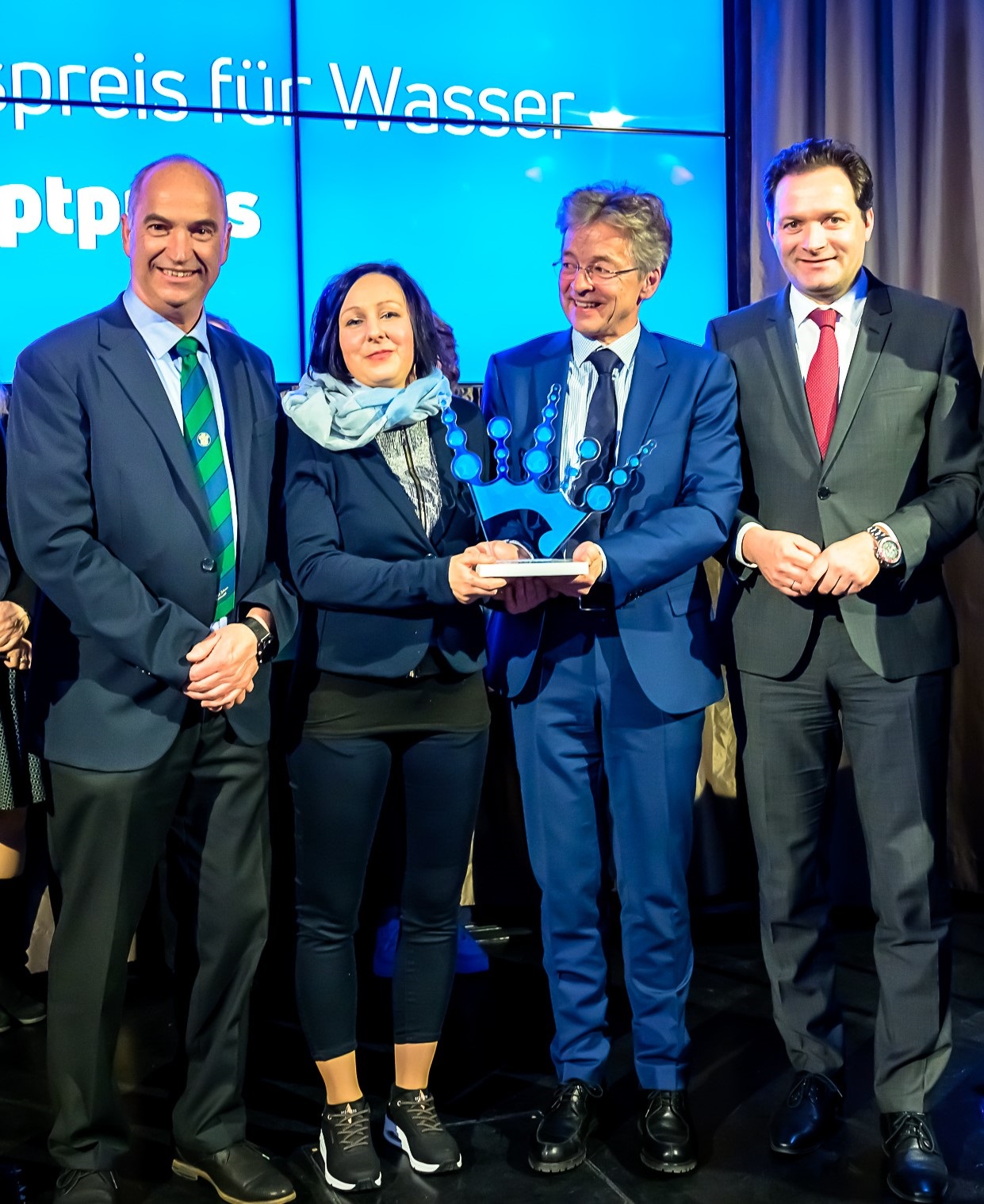 Vier Personen präsentieren stolz den Neptun-Staatspreis für Wasser vor einer blauen Hintergrundwand.