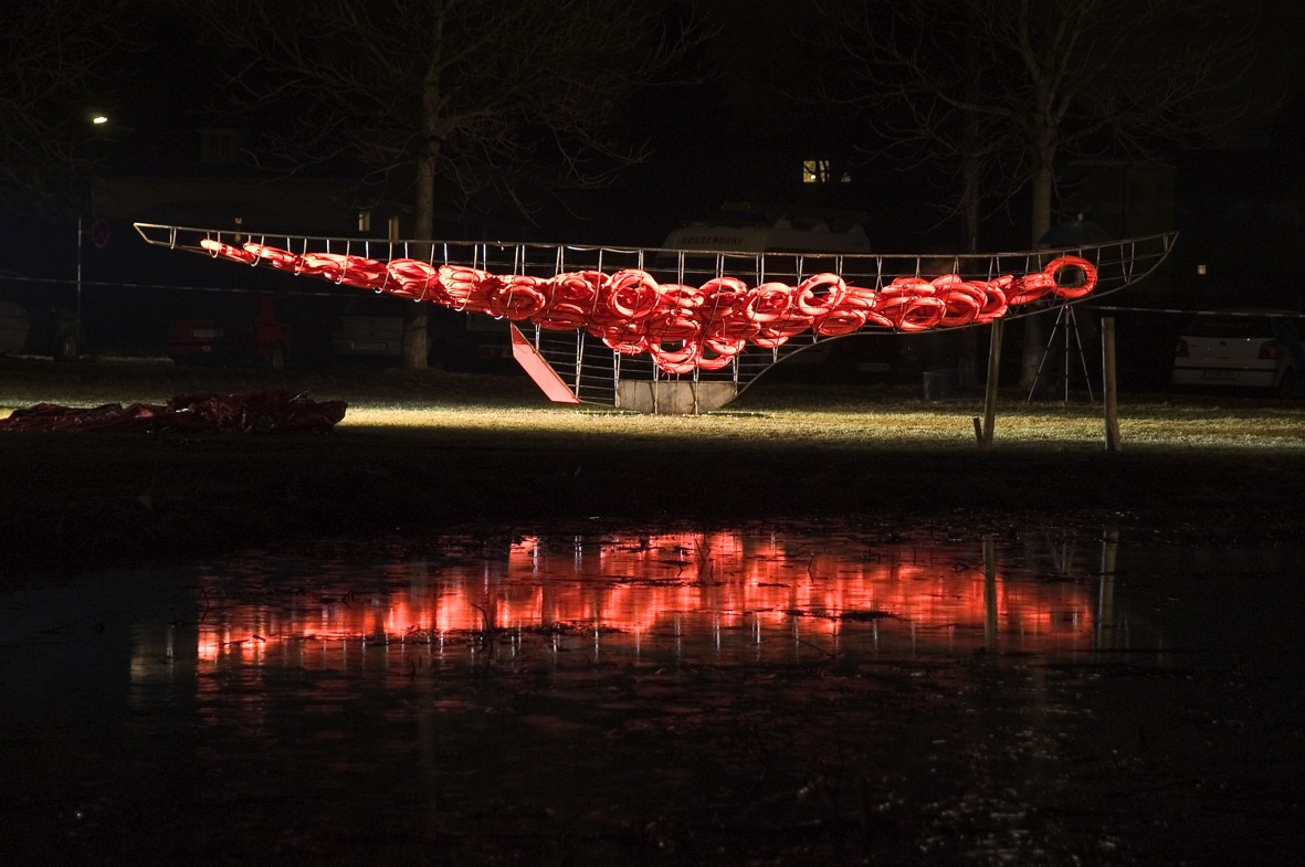 Beleuchtete Kunstinstallation mit Rettungsringen in einem Park, reflektiert in einem Wasserbecken.