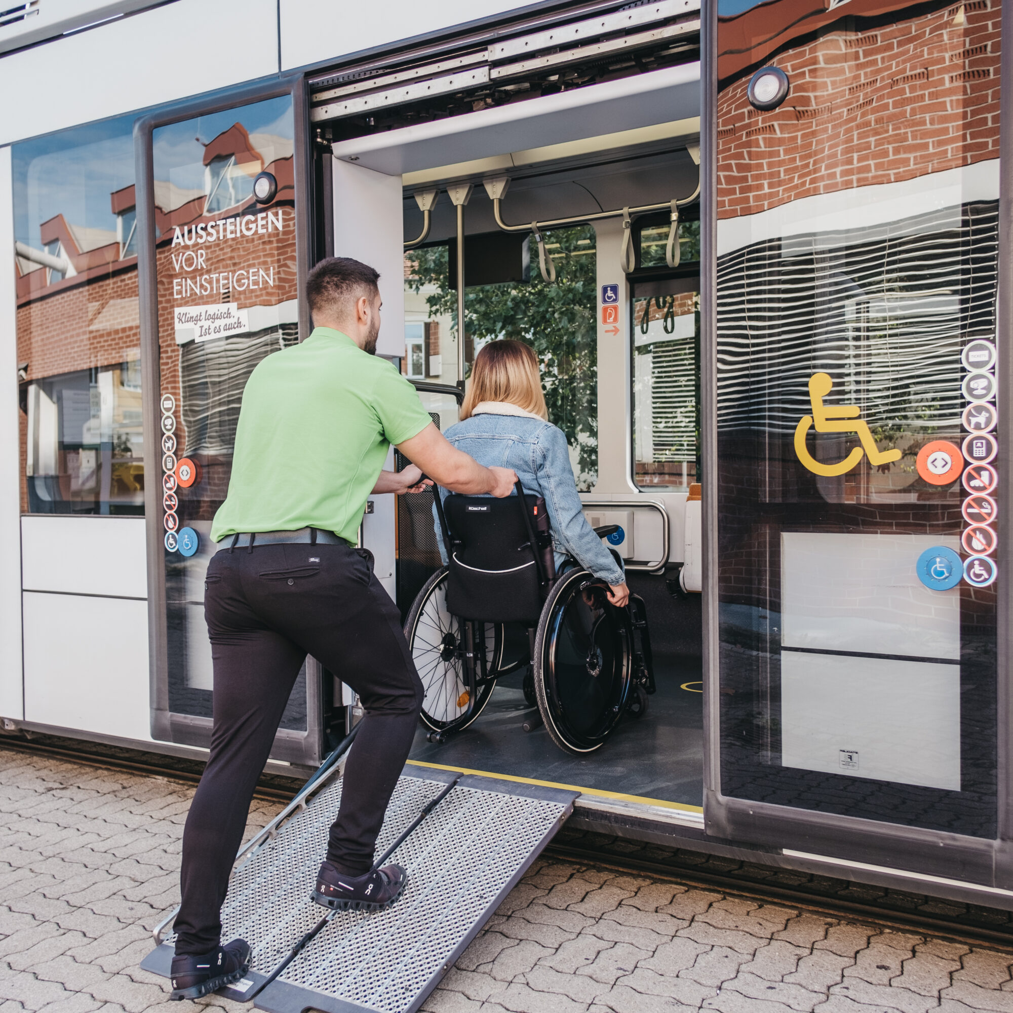 A man pushes a woman in a wheelchair up a ramp into a tram.