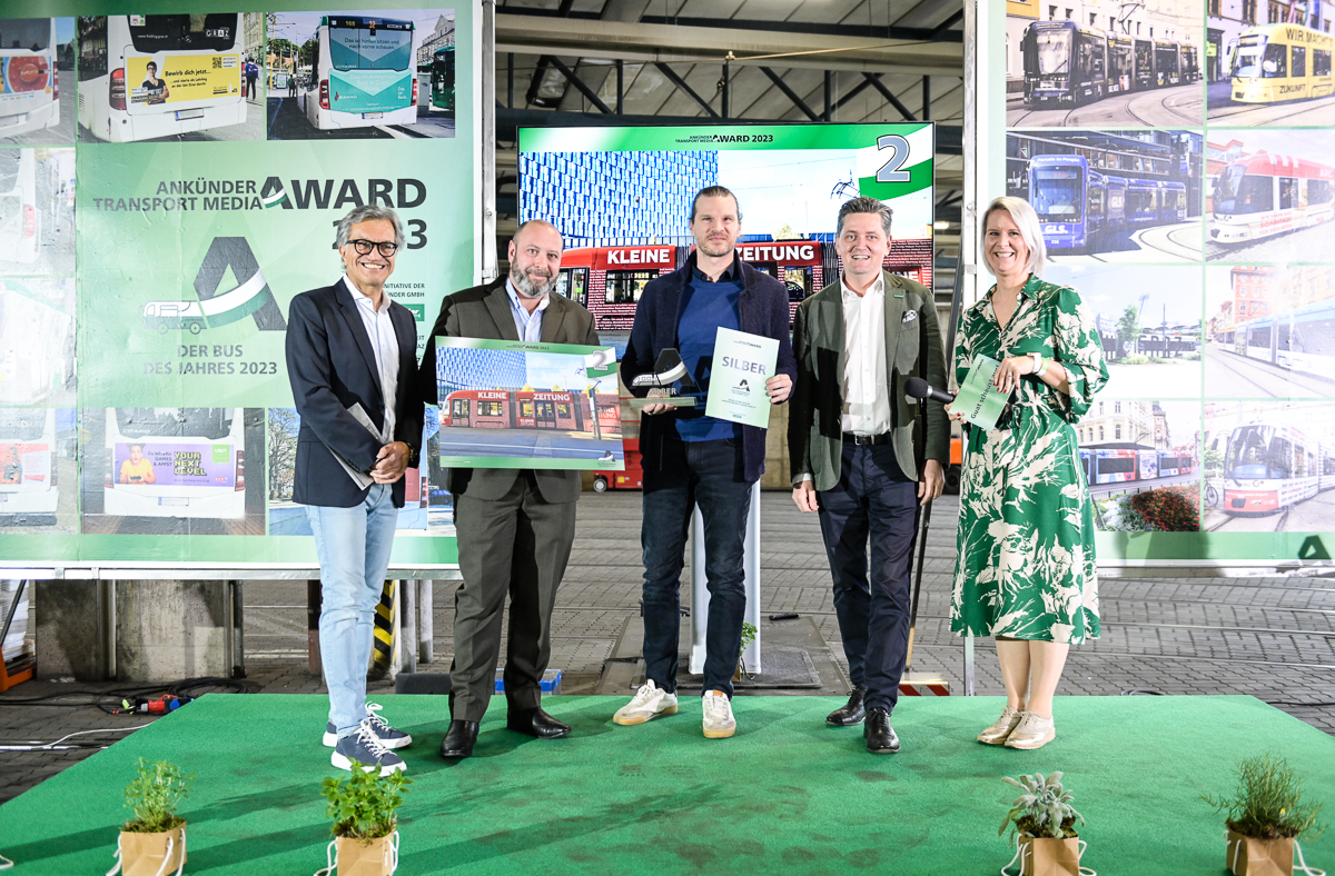 Personengruppe präsentiert Auszeichnung vor grünem Hintergrund mit Fotos von öffentlichen Verkehrsmitteln.