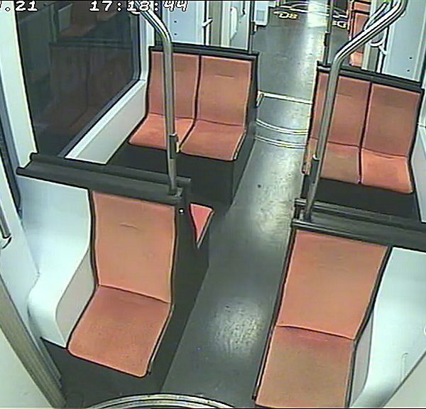 Empty train car interior with orange seats and handrails.