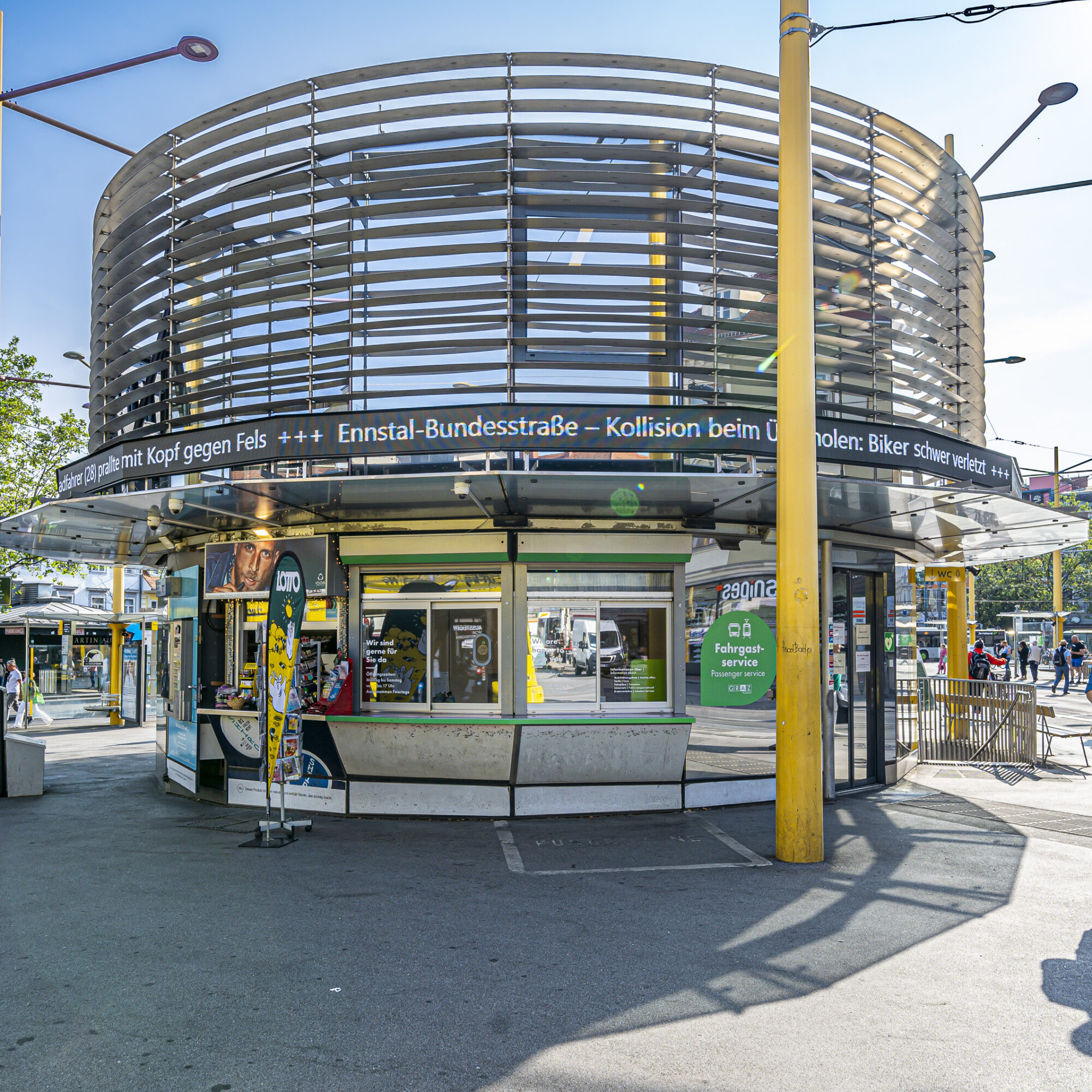 Rundes Fahrgastservice-Gebäude mit moderner Architektur und Anzeigetafel am Jakominiplatz in Graz.