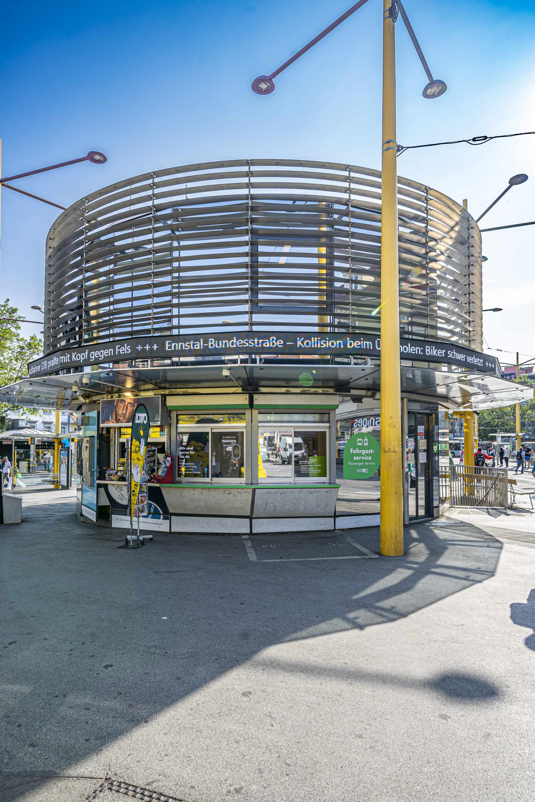 Rundes Fahrgastservice-Gebäude mit moderner Architektur und Anzeigetafel am Jakominiplatz in Graz.