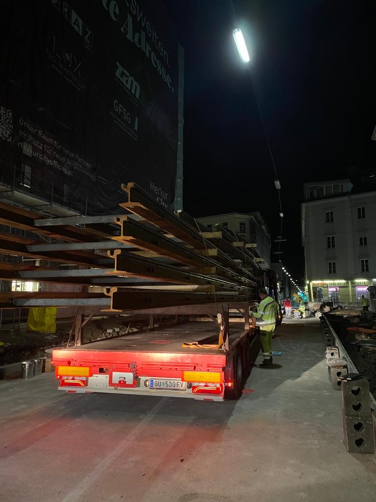 Nachtszene mit Bauarbeiten und einem LKW, der Schienen in der Neutorgasse transportiert.