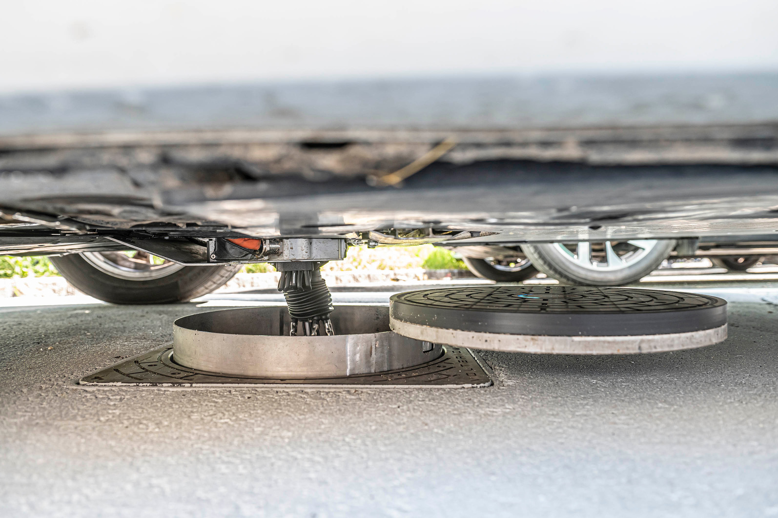 Detailansicht des automatisierten Ladeanschlusses unter einem Elektrofahrzeug auf einem Ladeplatz.