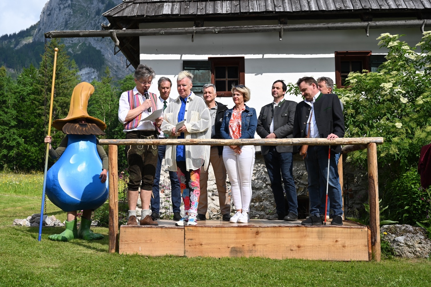 Personen auf einer Bühne bei einer Veranstaltung in ländlicher Umgebung, begleitet von einem Maskottchen.