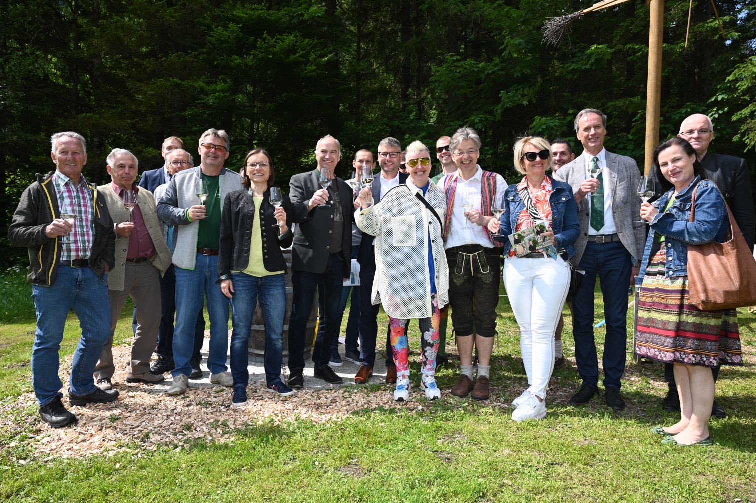 Gruppe von Menschen hält Gläser in der Hand, feierliche Atmosphäre im Grünen vor einer Waldkulisse.