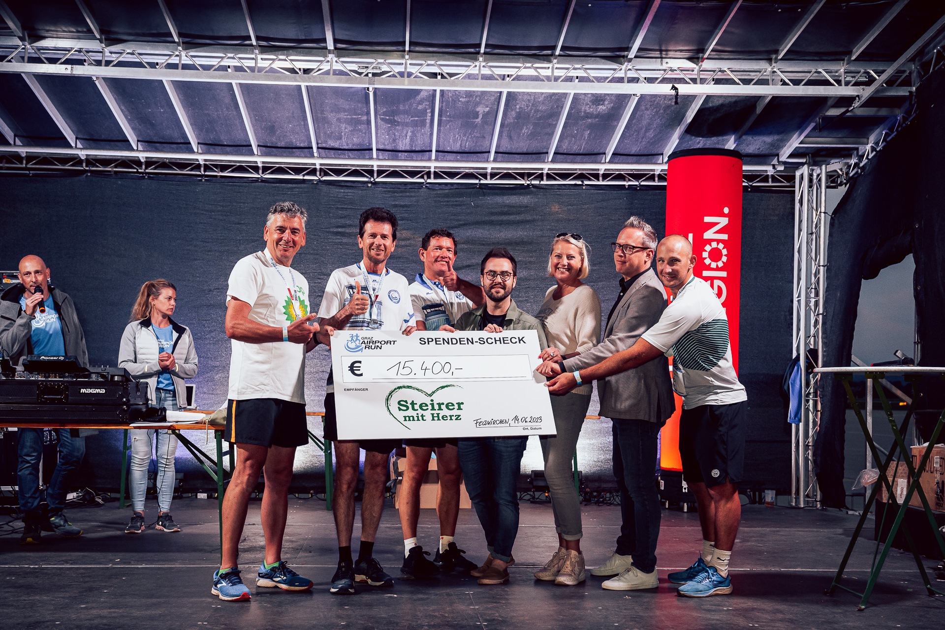 Scheckübergabe beim Graz Airport Run, Spendenbetrag 15.400 Euro, mit strahlenden Teilnehmenden.