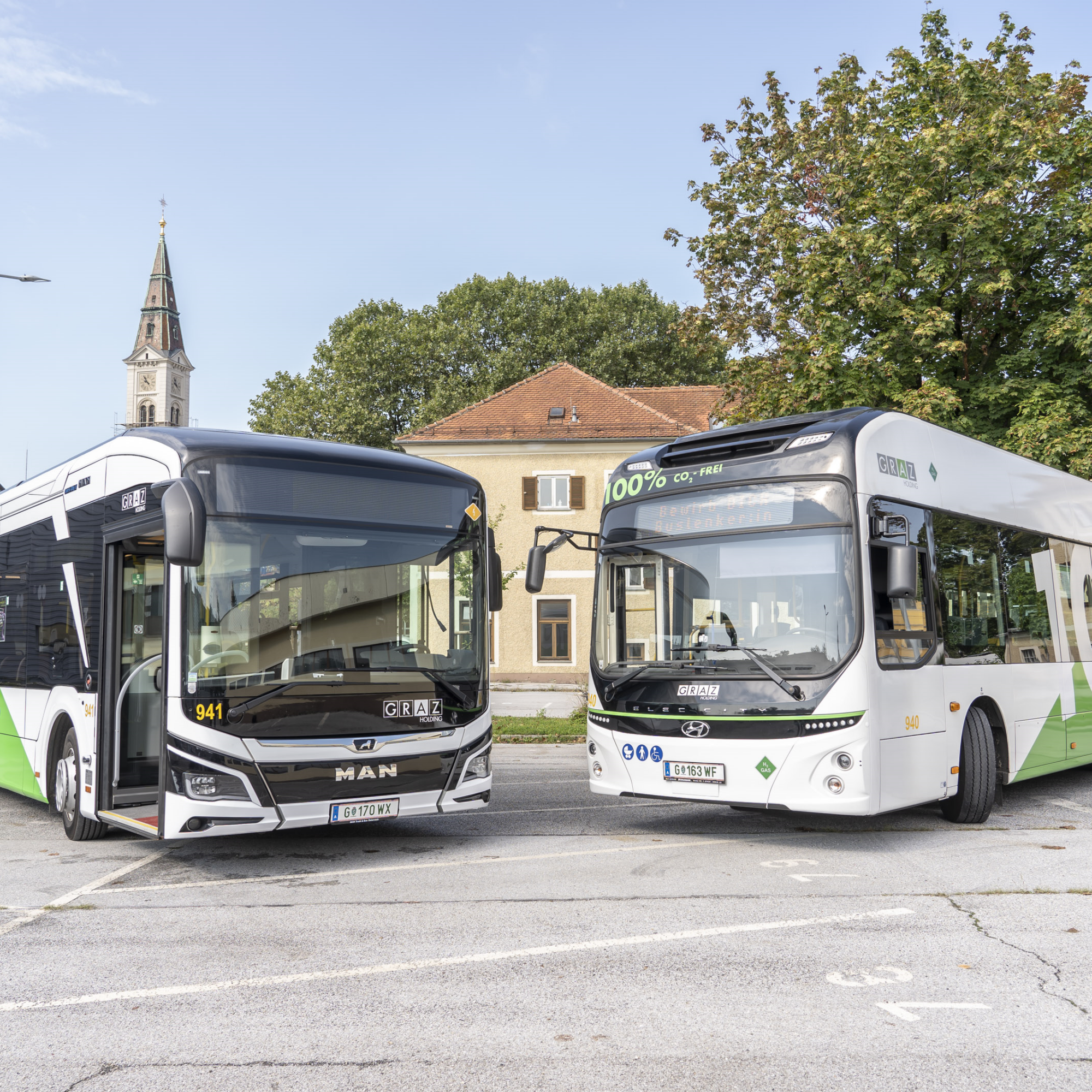 Gruppe vor zwei umweltfreundlichen Bussen mit Schildern zu 100% elektrisch und wasserstoffbetrieben.