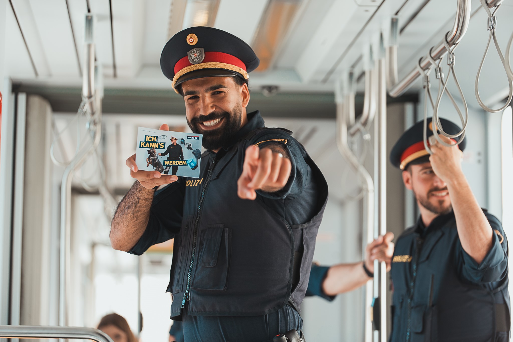Lächelnder Polizist in Uniform in der Straßenbahn zeigt Karte mit der Aufschrift „Ich kann’s werden“.
