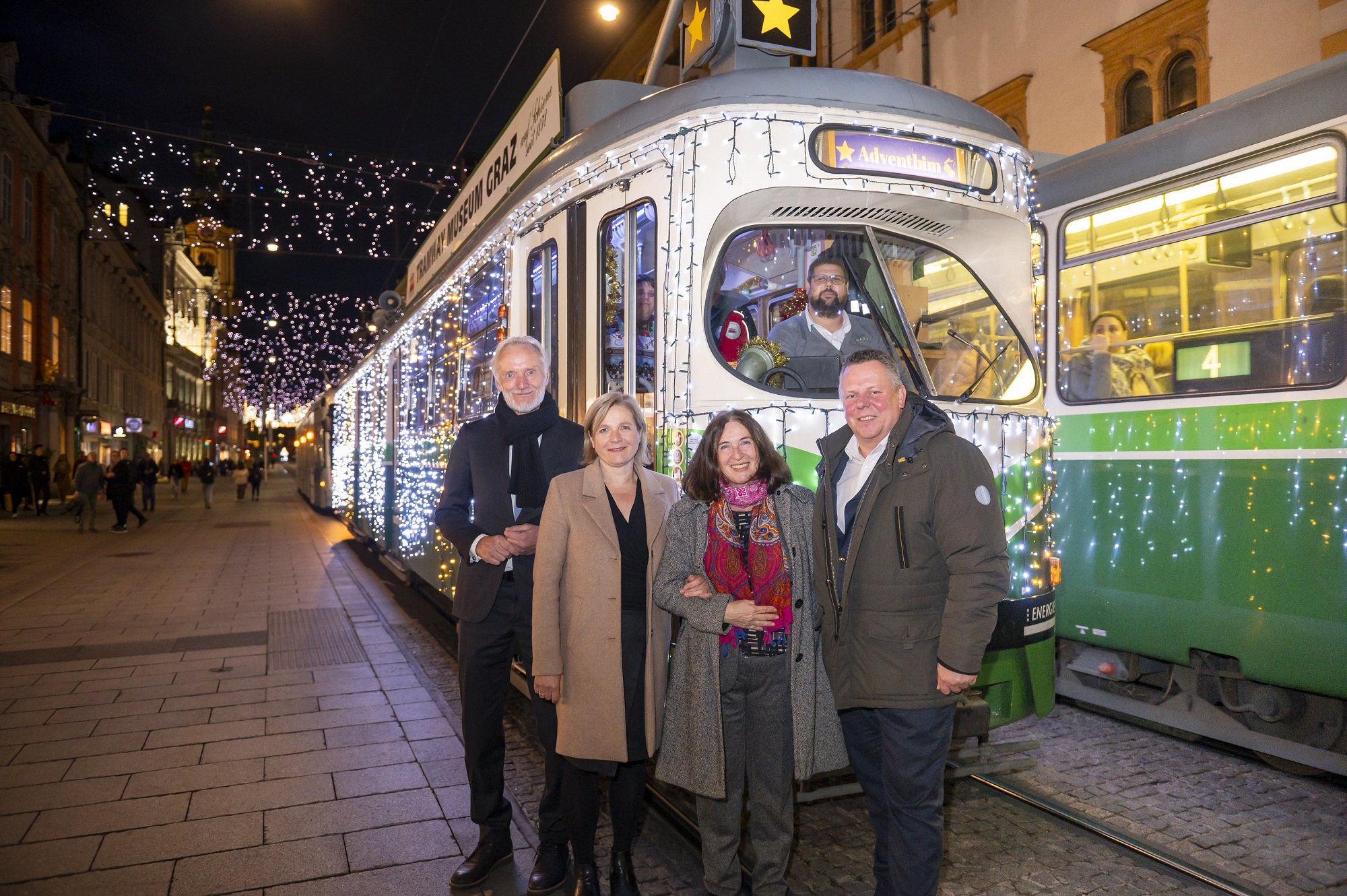 Gruppe vor beleuchteter Straßenbahn mit Aufschrift "Adventbim" in weihnachtlich dekorierter Straße.