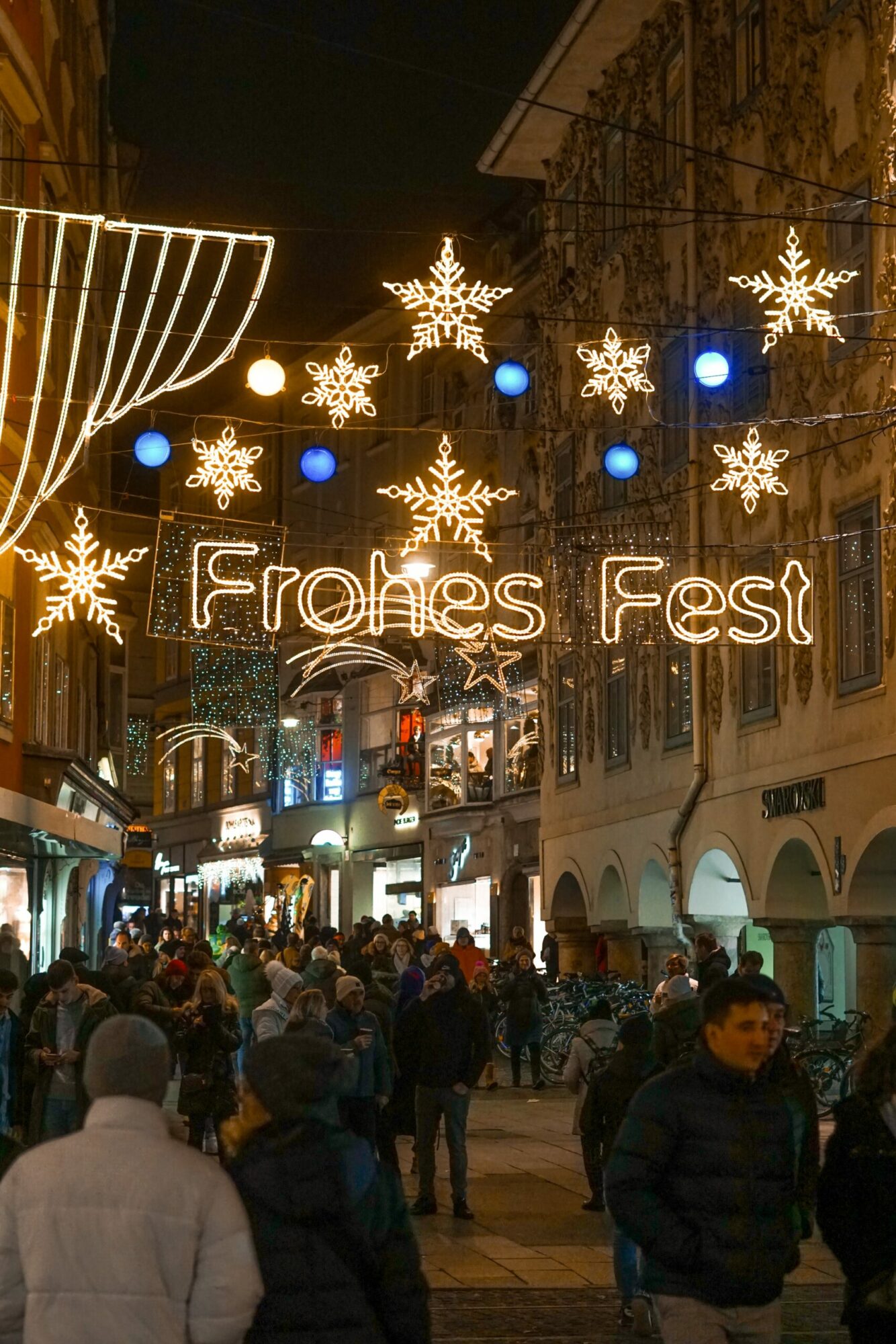 Beleuchtete Weihnachtsdeko mit Aufschrift "Frohes Fest" über Menschenmenge in Grazer Innenstadt.