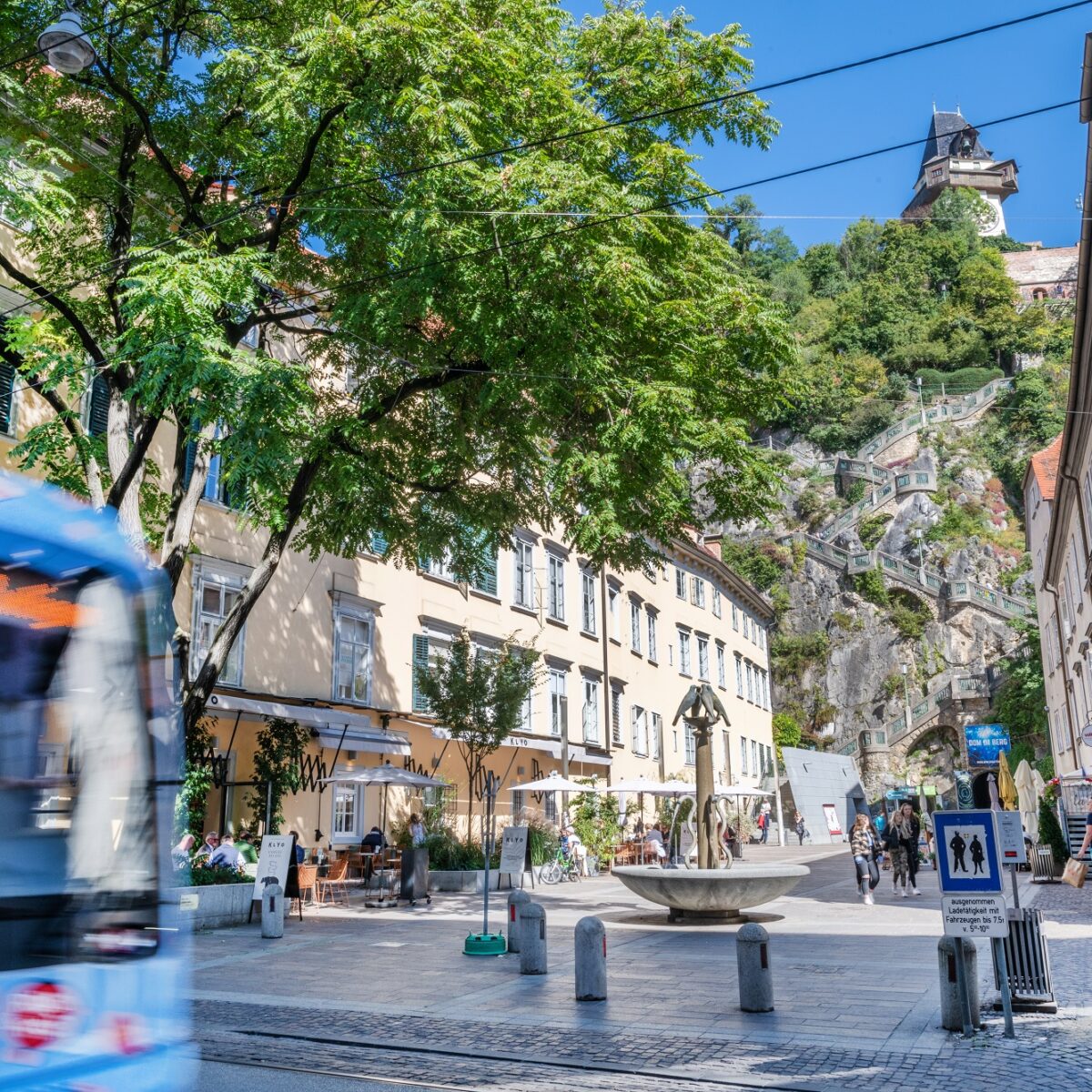 Straßenbahn fährt am Schloßbergplatz in Graz vorbei, im Hintergrund der Uhrturm.