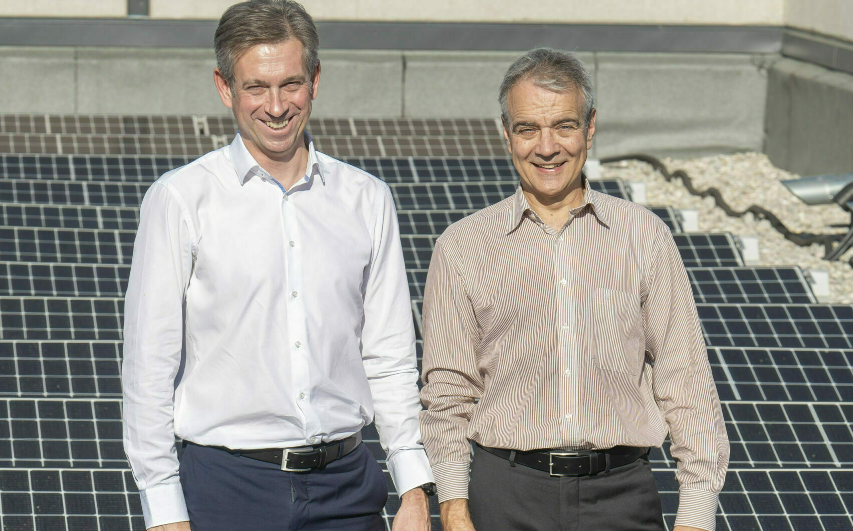 Zwei Männer stehen lächelnd vor einer Photovoltaik-Anlage.