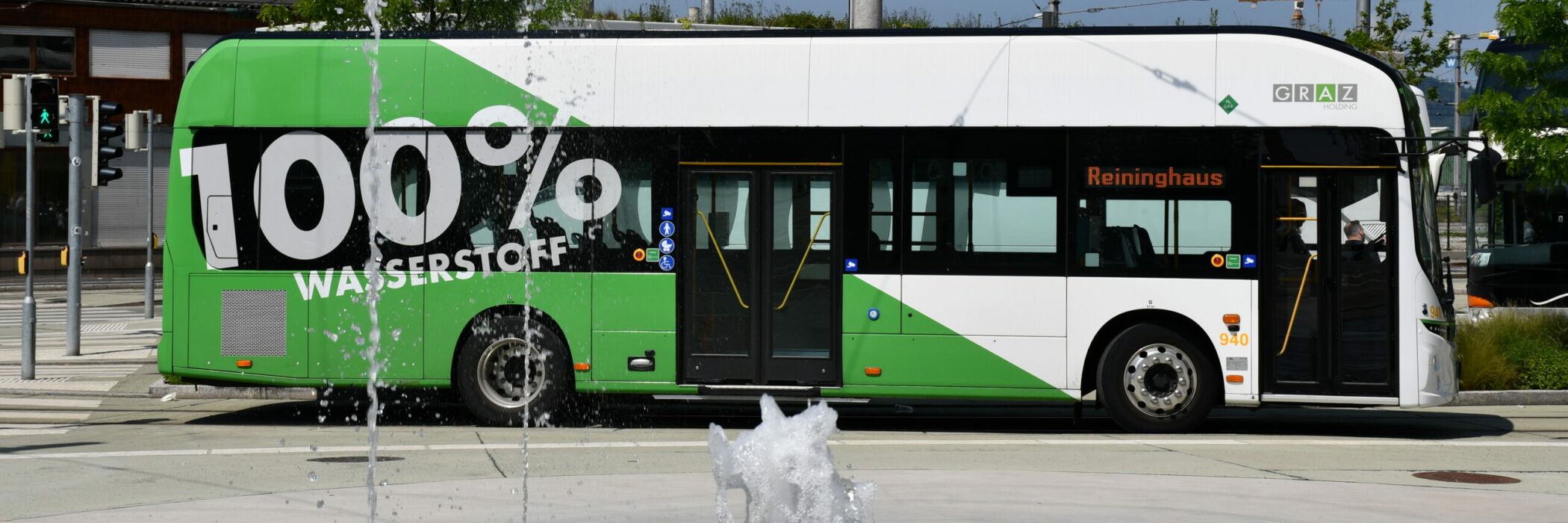 Ein weiß-grüner Wasserstoffbus der Graz Linien mit der Aufschrift "100% Wasserstoff" steht an Haltestelle.